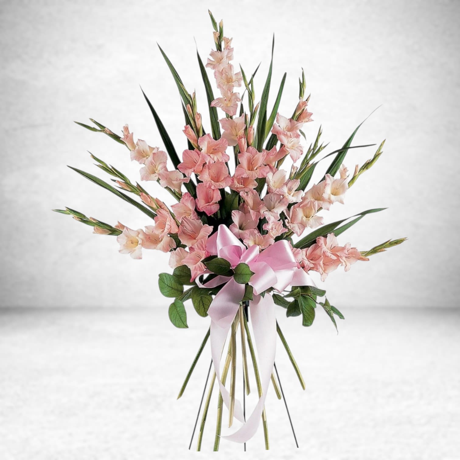 Blush Ascension Standing Spray Blush Ascension Standing Spray - Honor a life filled with grace and love with the Blush Ascension Standing Spray. Designed with elegance and tenderness in mind, this sympathy spray features tall, blooming pink gladiolus arranged with lush greenery and a soft pink satin bow. This standing tribute brings a message of serenity and hope to any funeral service, memorial, or graveside ceremony. Ideal for expressing heartfelt condolences, this classic pink floral design offers a timeless gesture of remembrance. Available for same-day funeral flower delivery in Houston, The Woodlands, Conroe, and surrounding areas by Twigs and Blooms. Substitution Policy: We take great pride in using the freshest flowers available. On rare occasions, specific stems or colors may be substituted due to local market availability. We always maintain the overall style, color palette, and integrity of the arrangement to ensure it remains a meaningful tribute.