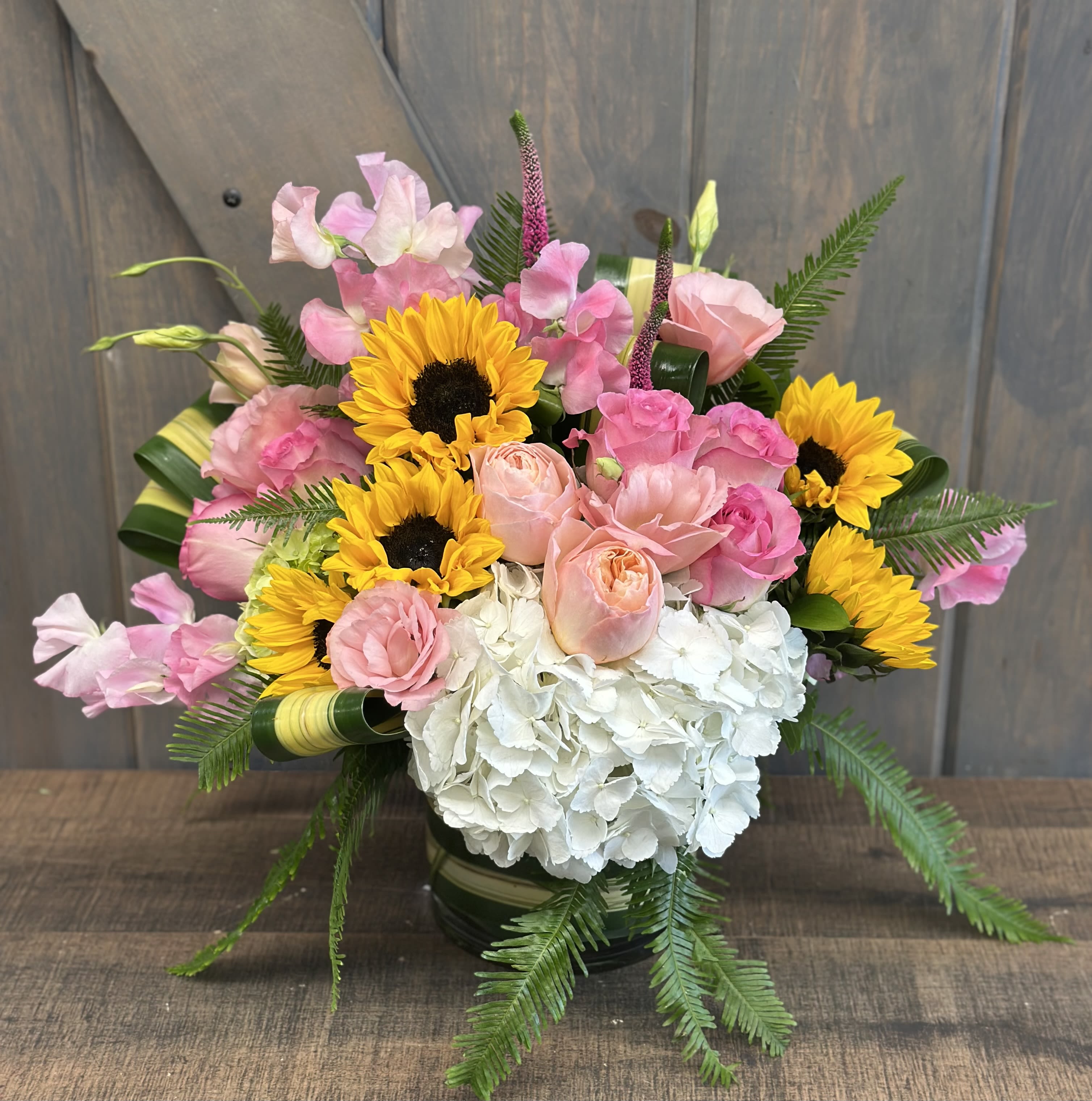 Summer Romance Summer Romance - Bright, light, soft, and absolutely perfect for any occasion, but especially great for lifting spirits! Included in this design are Garden Roses, Hydrangea, Roses, Mini Hydrangea, Sunflowers, Lisianthius, Veronica, Sweet Peas, Umbrella fern, and Flax leaf