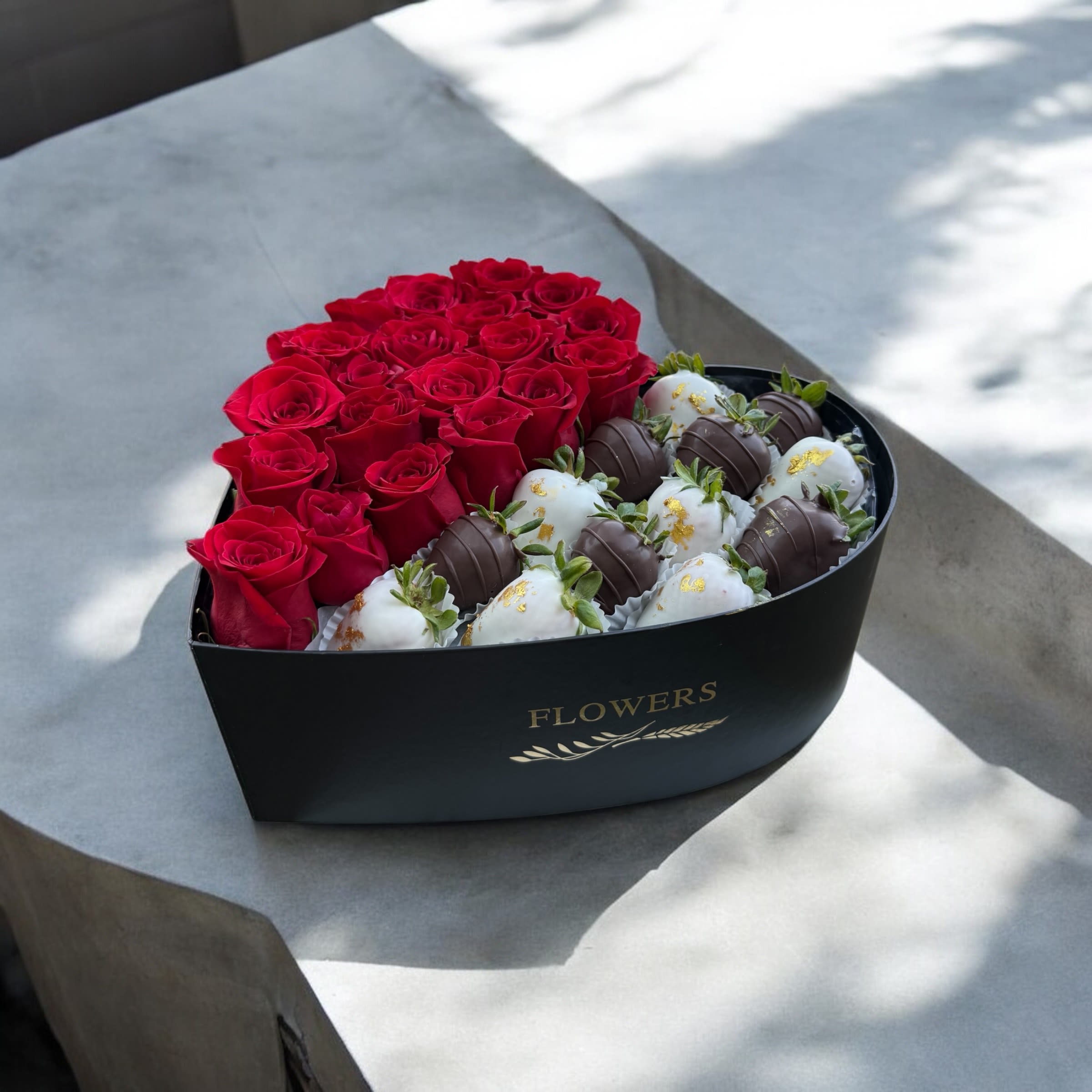 Corazón Imperial - A luxurious black heart-shaped box. One half filled with 24 bold red roses that speak of passion and deep love; the other half, a gourmet selection of organic strawberries dipped in dark, white, and marbled chocolate, adorned with golden touches. A floral and sweet experience designed to impress. Love, redefined in luxury. 