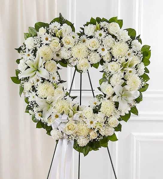 Floral Heart Tribute- White - Open, heart-shaped arrangement of all white roses, hybrid lilies, football mums, carnations and daisy poms; accented with baby’s breath and soft, lush greenery