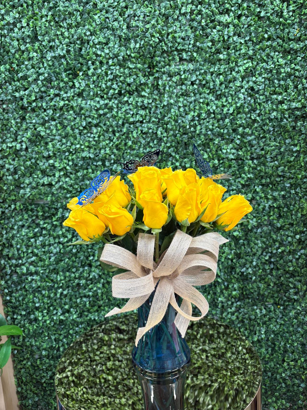 Sunlight &amp; Wings - A bouquet that radiates joy and freshness. 25 bright yellow roses that symbolize friendship, gratitude and new beginnings, accompanied by delicate butterflies that give it a magical and special touch.  Presented in a glass vase and adorned with a rustic bow that enhances its natural charm.