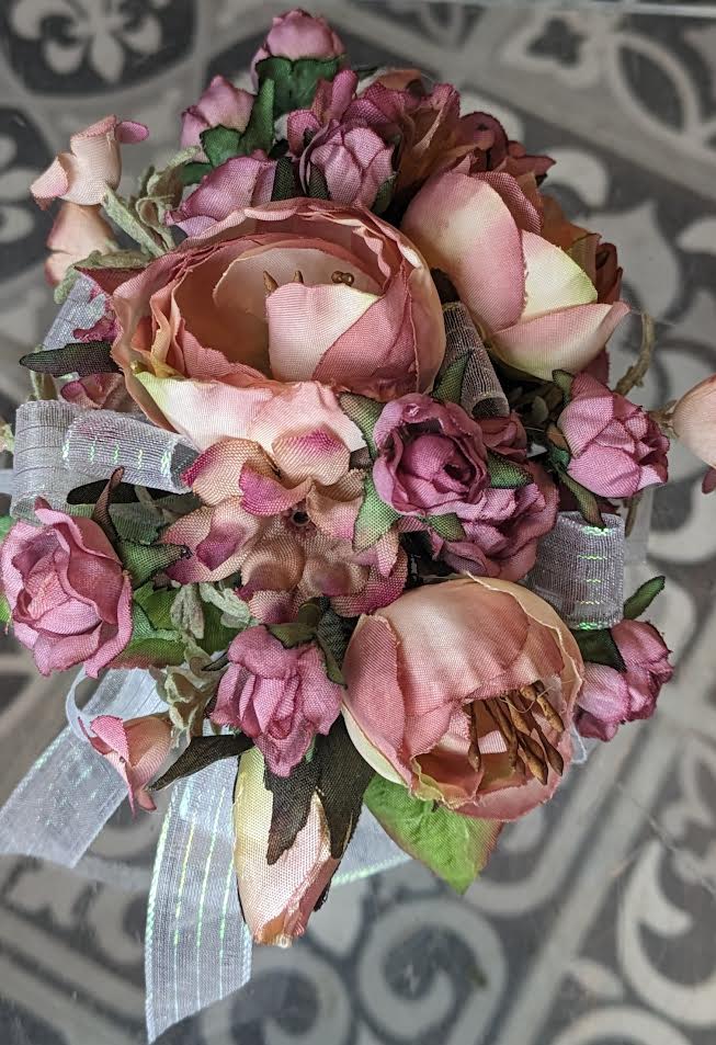 Modish Mauve Silk Wrist Corsage Modish Mauve Silk Wrist Corsage - These are artificial flowers. The flowers and ribbon cannot be changed. It is currently on a white snap band but can be put on a black, silver or gold snap band if needed, if they are available.