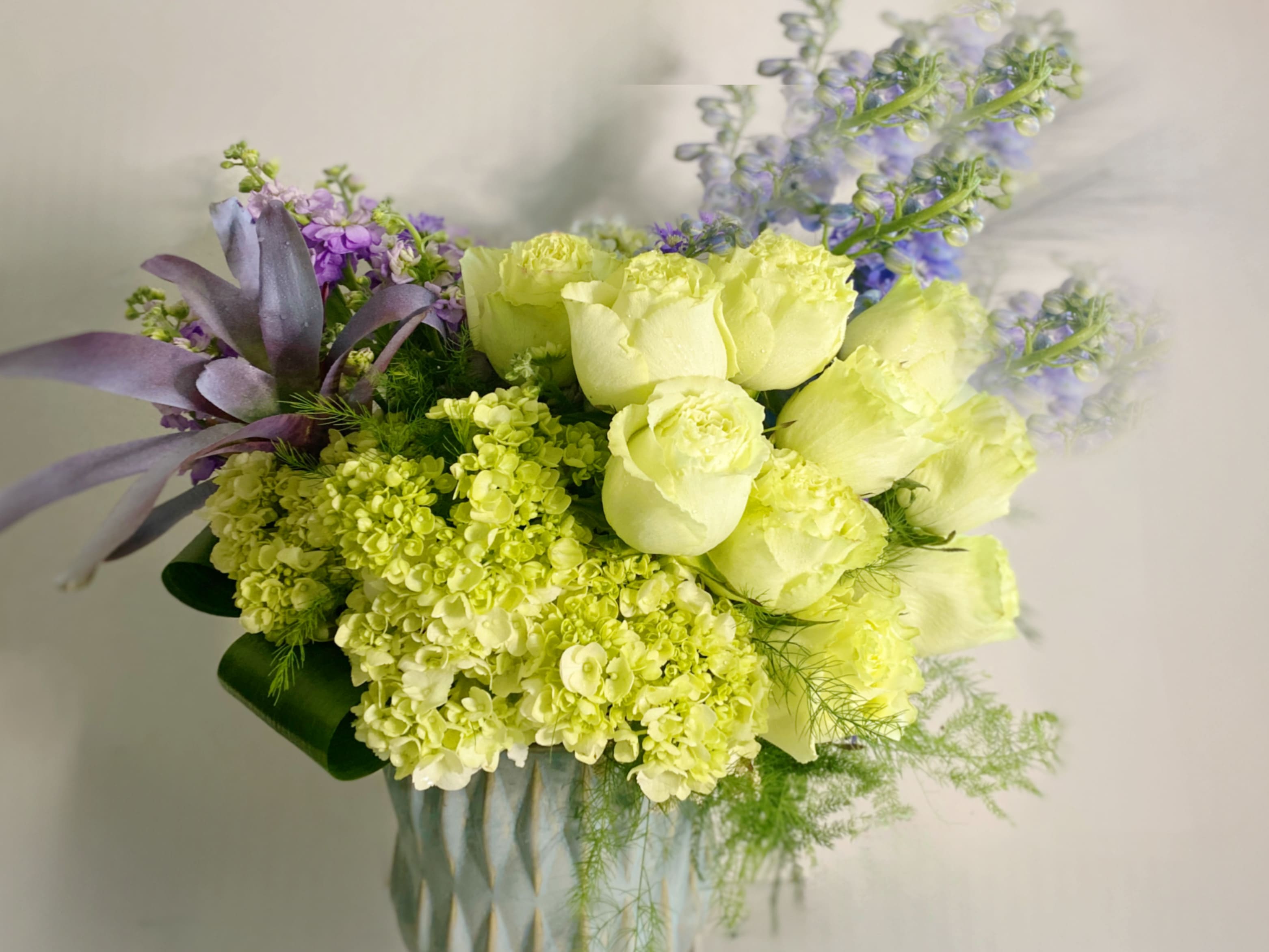 Azure on Green - Azure on Green adorning a grouping of 2 dozen green roses with hints of baby blue and periwinkle flowers in an azure ceramic. This is a lush clean design that is color blocked. This floral arrangement is simply luxurious and stunning. This modern design speaks tranquility,peace, comfort and celebration. It’s a perfect gift for a new baby, congratulations and sympathy. Approximately 15x15 