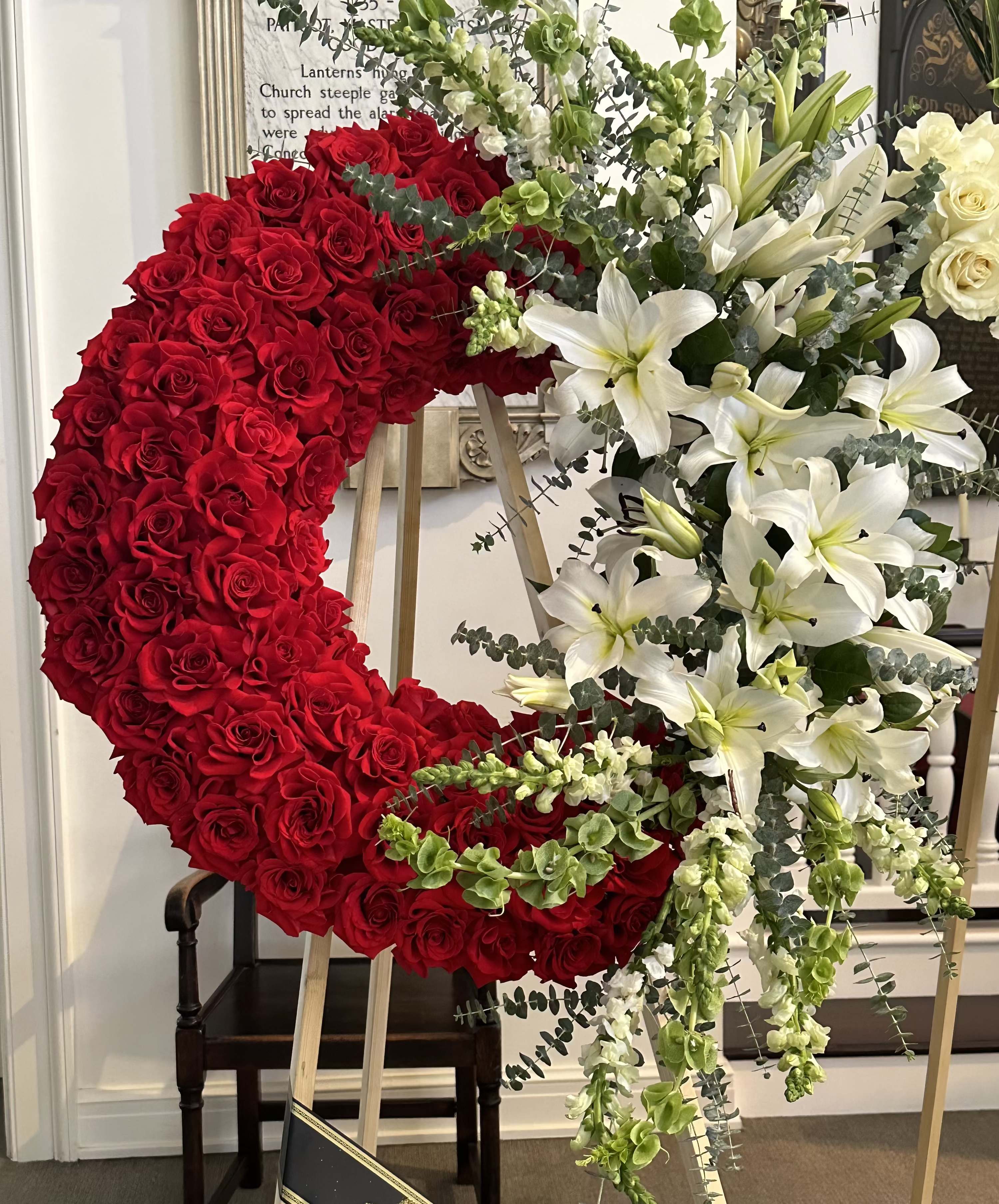 Roses and Lilies Wreath By VLM Flowers - The Roses and Lilies wreath is classic. It is made of red roses and white lilies. The wreath has an accent on the top right corner of the lilies, snapdragons, and bells. The picture represents the premium price of a wreath.