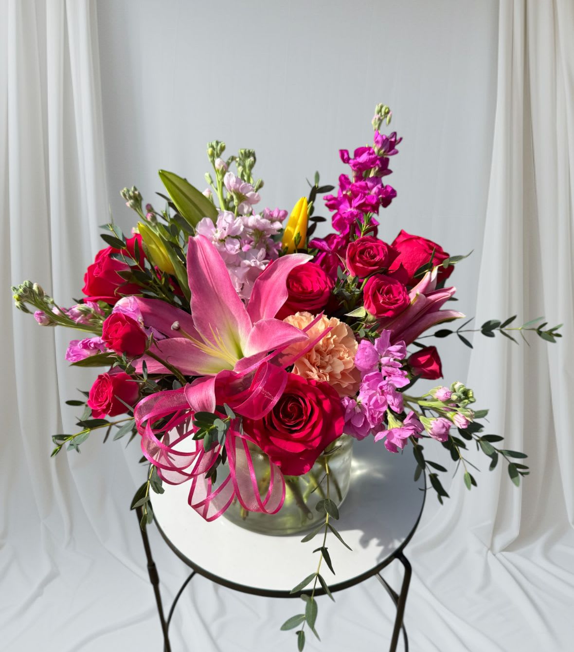 Mamma Mia Mamma Mia - Elegant design using bursts of vibrant pink flowers such as roses, lilies and stock. Accented with filler flowers and premium greenery. Vase Dimensions: 6" x 6" Overall size: 12" x 12"