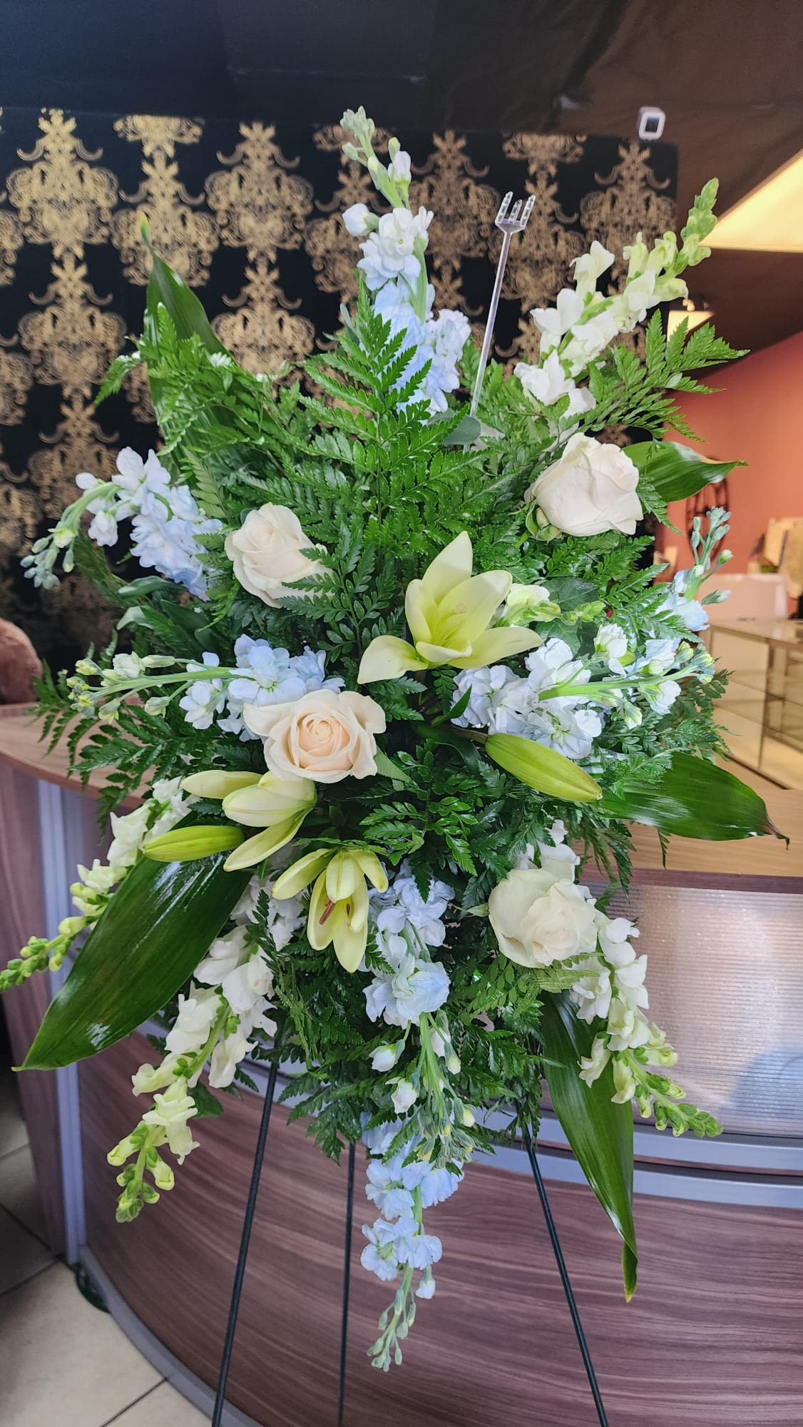 Blue Standing Spray  - Express your sympathy with this blue standing spray that contains white roses, lilies, stock, and blue stock with greenery. 