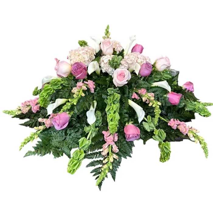 Enchanted Garden Casket Spray - A serene blend of pink hydrangeas and roses, accompanied by snapdragons, bells of Ireland, and white calla lilies. Each flower holds memories of love and beauty, creating a peaceful tribute to a cherished life.