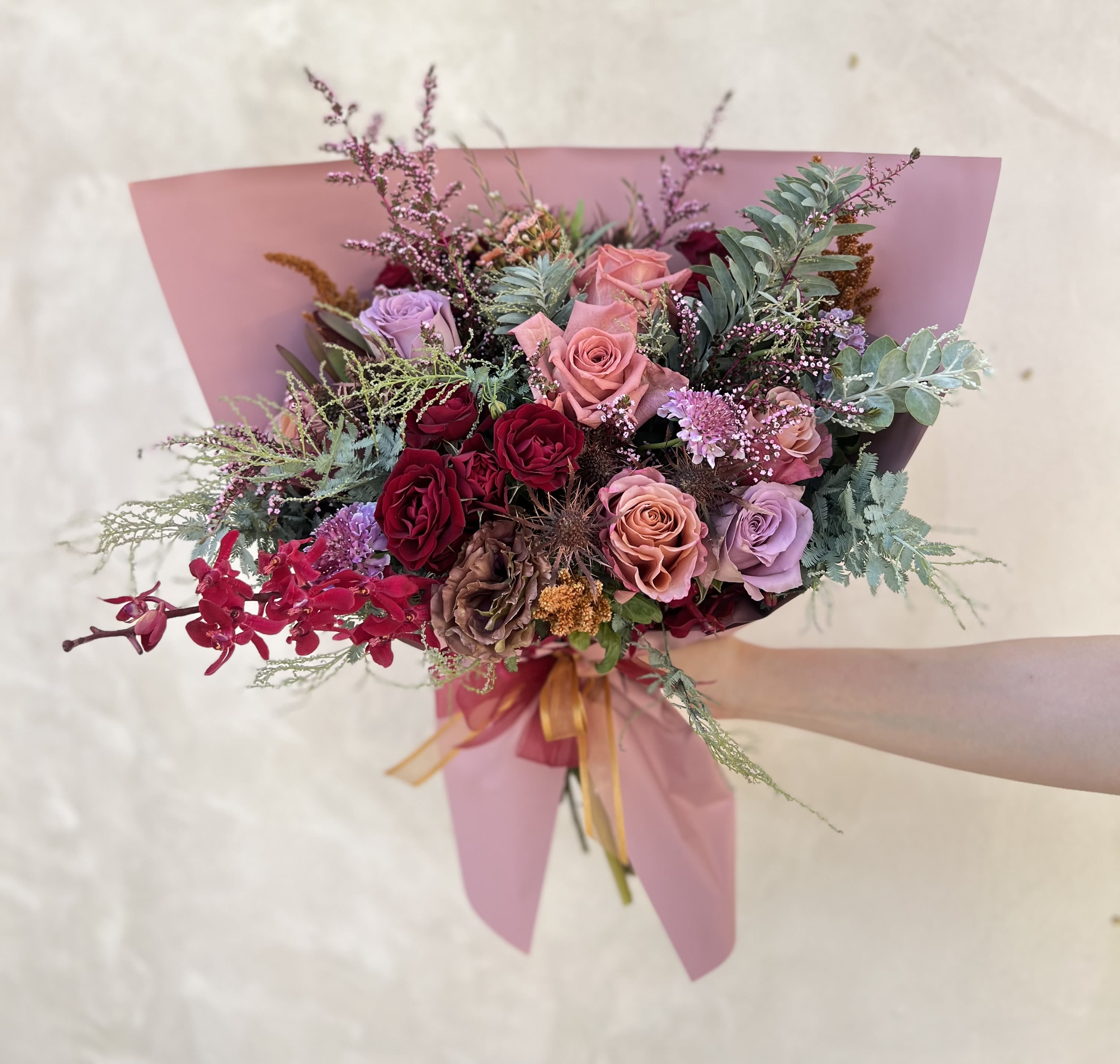 American Dawn - Flowers: purple moon roses, amnesia roses, barista roses, mauve scabiosa, mauve lisianthus, gold amaranthus, acacia greenery, azimah red orchids, pink calcynia, burgdundy spray roses, and gold thistles.  Wrapped in mauve paper, gift wrapped with a burgundy and gold ribbon. 