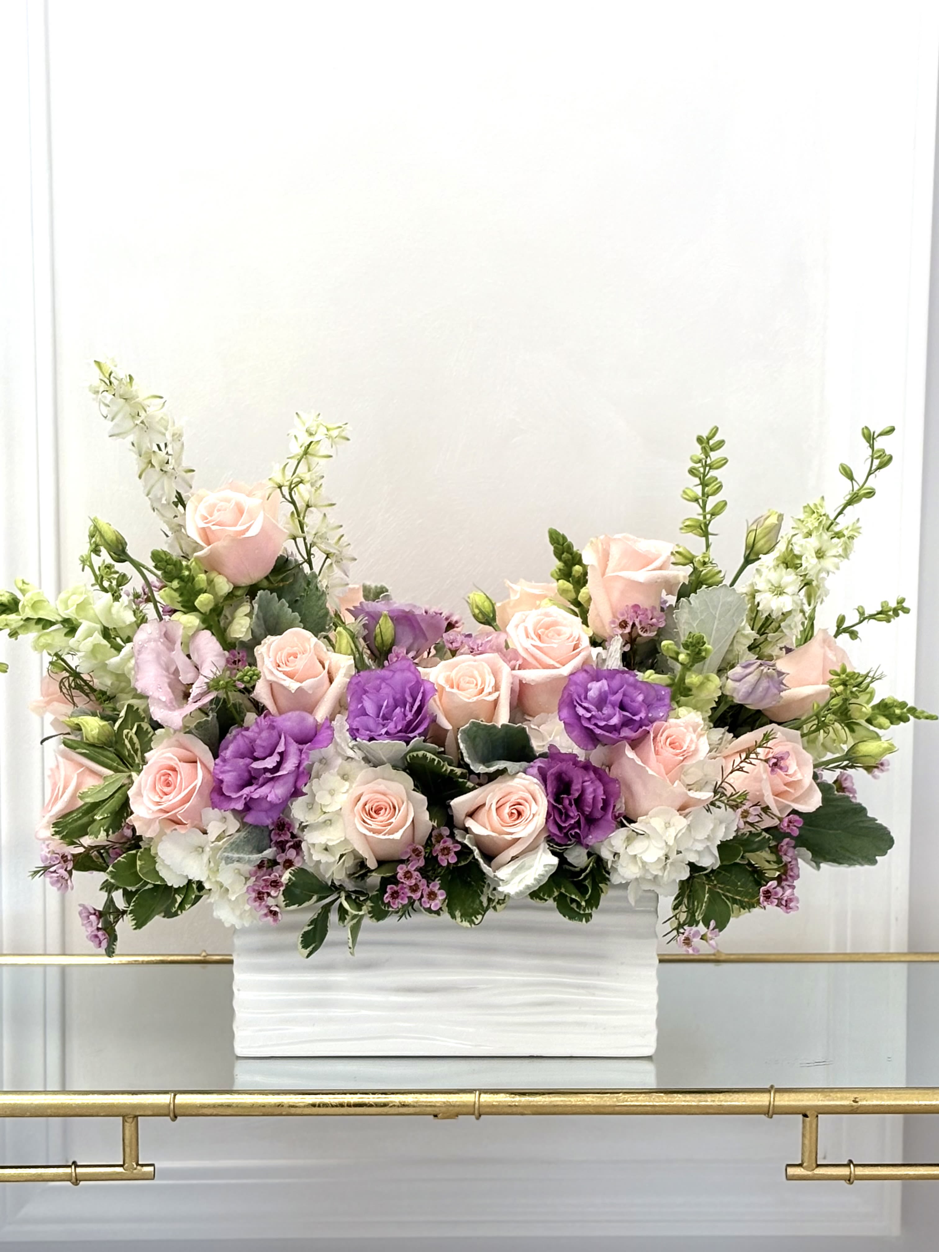 Garden Sonata By VLM Flowers - Like a gentle sonata in bloom, this arrangement weaves together pastel florals in a harmonious palette. Featuring fresh garden roses, lavender tones, and white seasonal flowers in a modern white ceramic container, Garden Sonata is perfect for expressing love, sympathy, or grace.