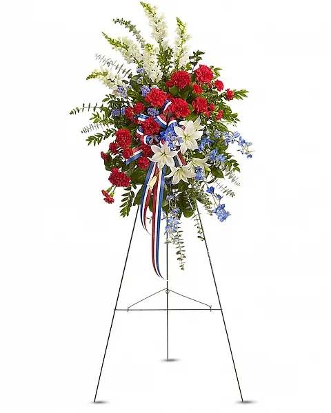 Sacred Duty Spray - Standing tall, proud and patriotic, this dazzling free-standing spray is like a fireworks display made of graceful flowers. Uniquely beautiful, it's a lovely way to honor a great loss.  A gorgeous selection of flowers such as white lilies and snapdragons, blue delphinium, red carnations and miniature carnations, eucalyptus and more create this all-American spray.