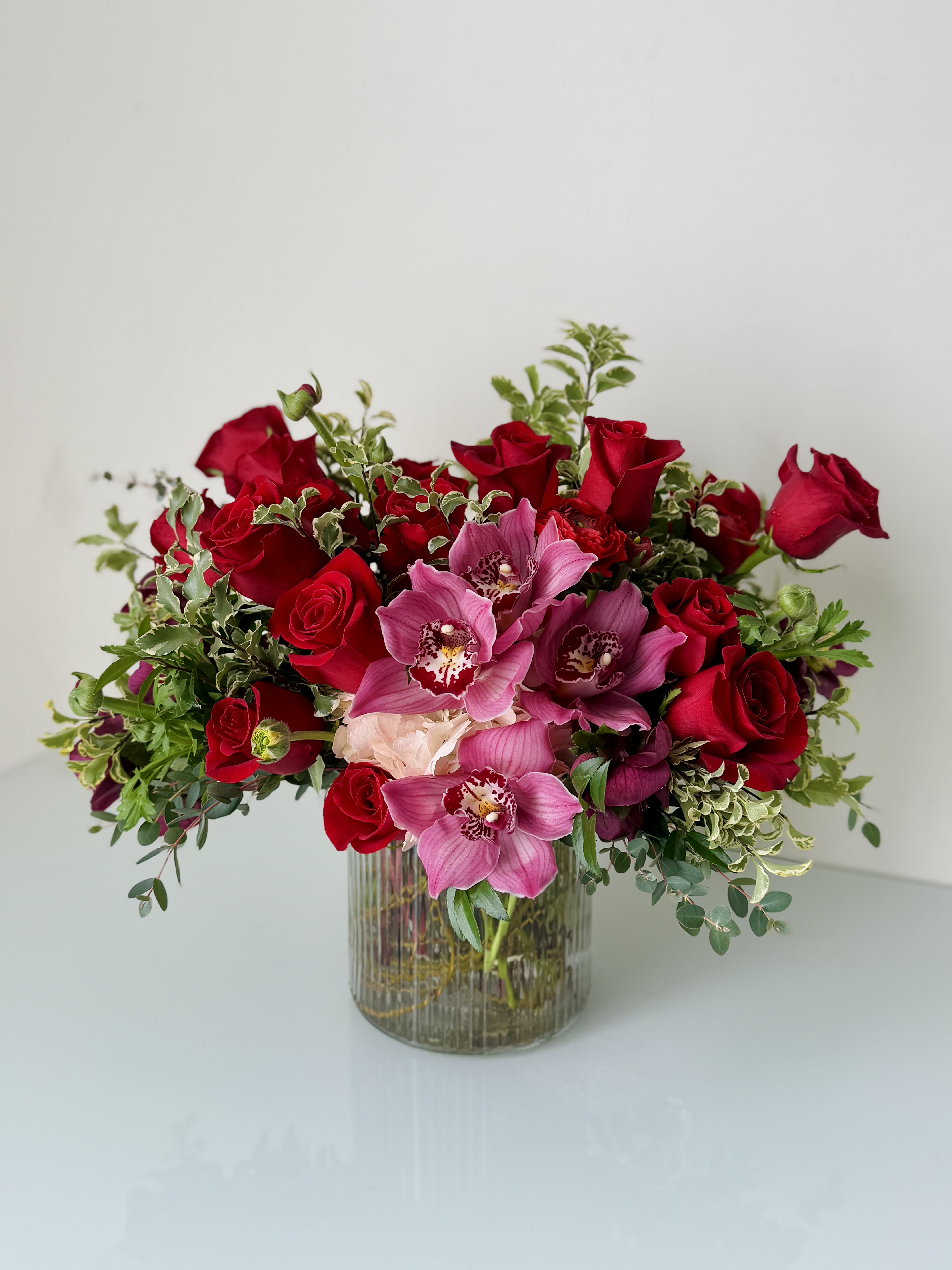 Love Story Love Story - Beautiful one-sided flower arrangement with red mix blooms. Roses and cymbidium orchids are the main flowers. This arrangement is built in 6x6 cylinder.