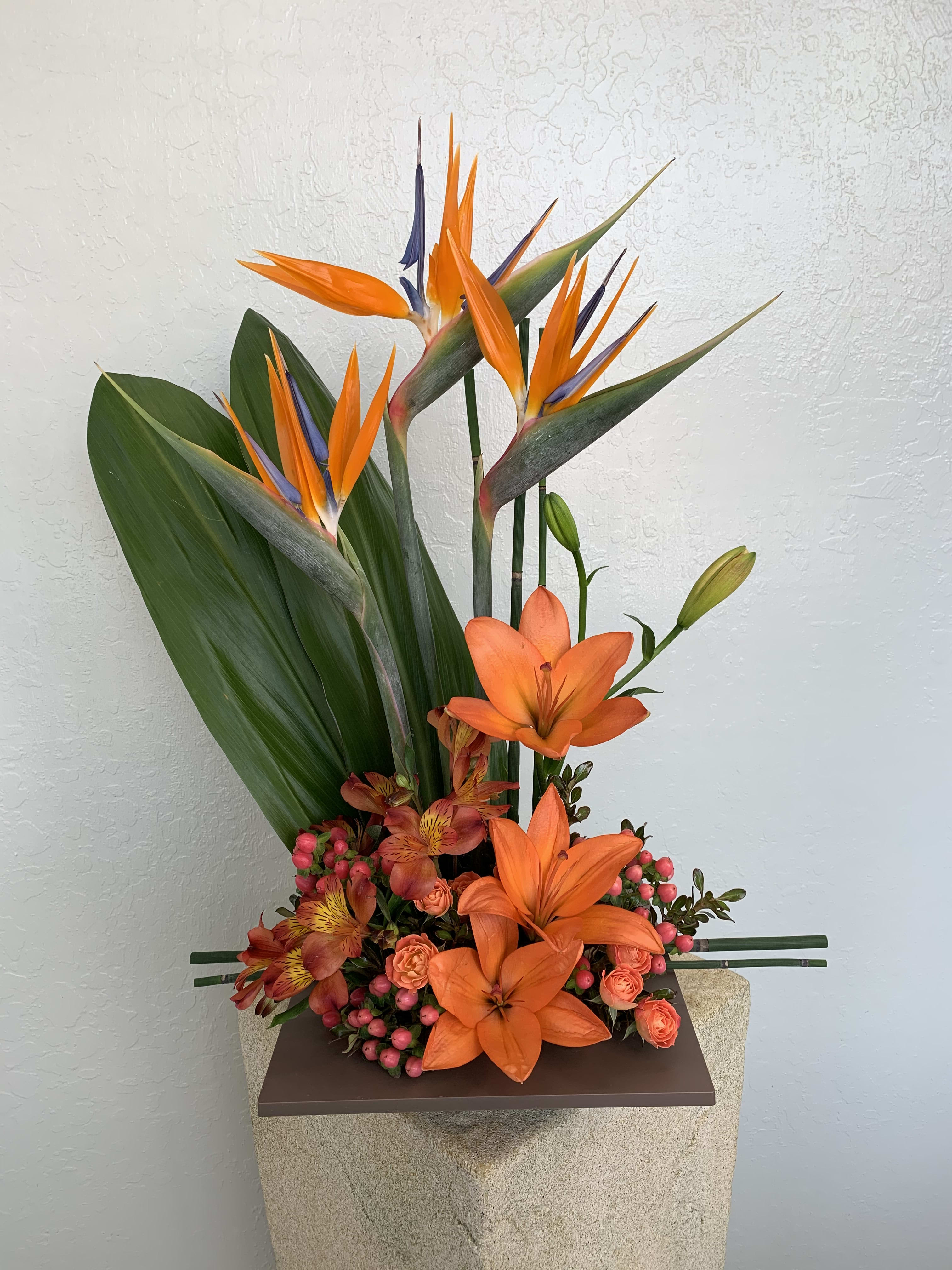 Birds of a Feather - Birds of a feather flock together with bird of paradise, orange lilies, alstroemeria, hypericum berries, and filling flowers all year round. Delivered in a red or dark brown bamboo dish. Orientation: One-Sided Approximately 24&quot;H x 16&quot;W