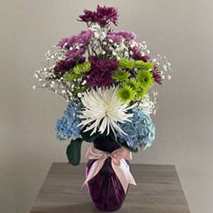 Daydream Lavender - Delightful bouquet of white Anastasia flowers, green dahlia flowers, baby’s breath flowers, pink and purple marguerite daisies and blue hydrangeas on a purple vase with a pink bow.