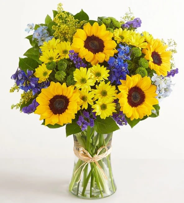 Sunny Days - Brighten that special someone's day through this arrangement that features. Sunflowers, blue delphiniums, yellow daisy poms, green button poms, and purple statice, accented with assorted greenery. 