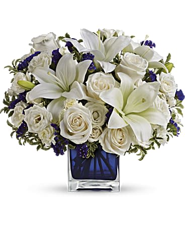 Sapphire Skies Bouquet/ Ramo de Cielos de Zafiro Sapphire Skies Bouquet/ Ramo de Cielos de Zafiro - Like gazing into a clear blue sky, this serene arrangement soothes the soul and cheers the heart. Its creamy roses and snowy lilies are arranged in our dazzling sapphire cube. Crème roses, white asiatic lilies and white miniature carnations are mixed with bursts of purple statice and green pitta negra. Delivered in Teleflora's glass Cube. Orientation: All-Around Mirando hacia un cielo azul claro, este sereno arreglo calma el alma y alegra el corazón. Sus rosas cremosas y lirios blancos están dispuestos en nuestro deslumbrante cubo de zafiro. Las rosas crème, los lirios asiáticos blancos y los claveles en miniatura blancos se mezclan con estallidos de statice púrpura y pitta negra verde. Entregado en el cubo de vidrio de Teleflora. SUBSTITUTION POLICY – Always deliver the freshest flowers! Please note the bouquet pictured reflects our original design. If the exact flowers or container in this arrangement are not available, our local florists will create a beautiful bouquet with the freshest available flowers.
