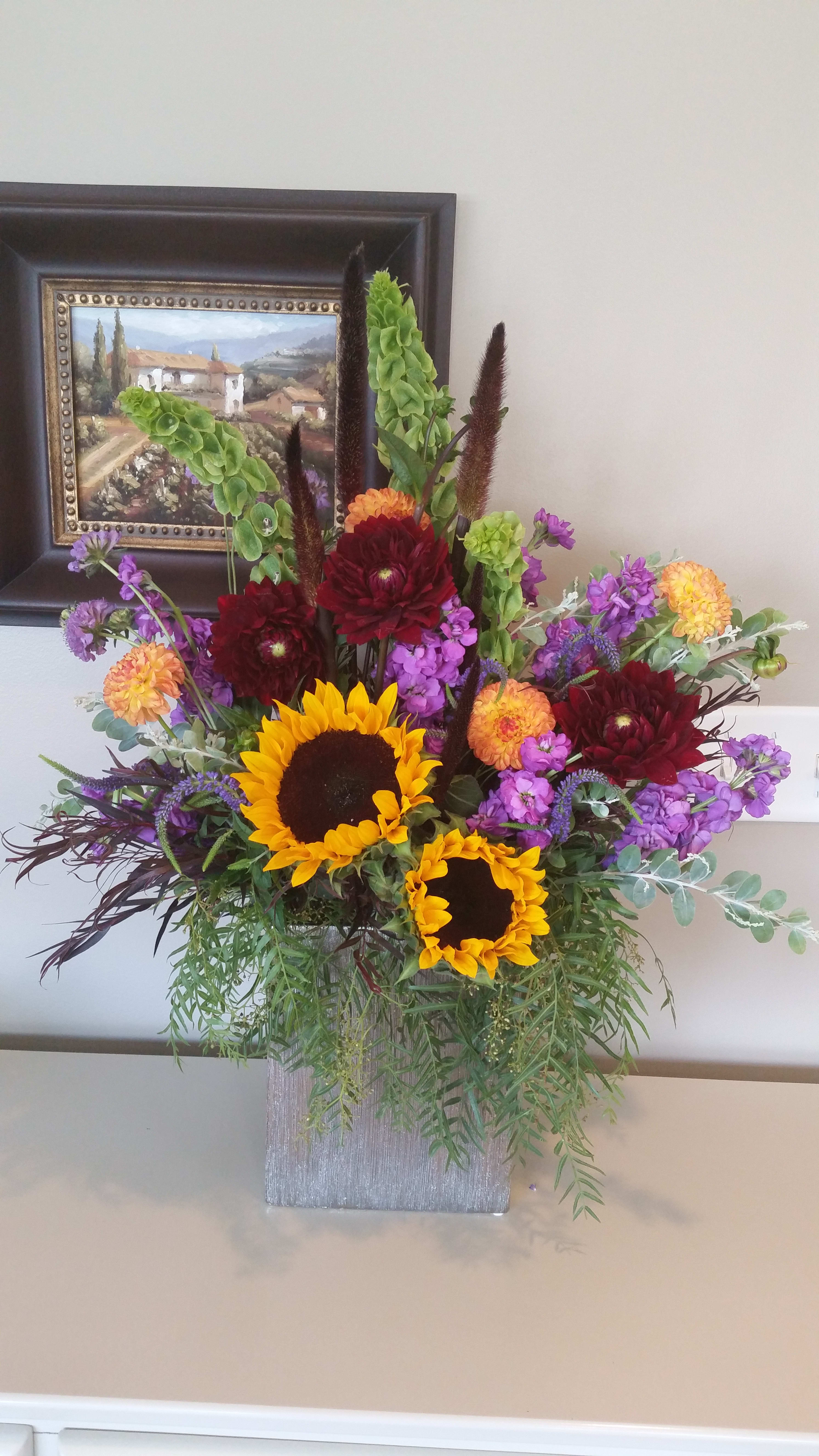 Mountain Meadows  - An arrangement full of color and texture arranged in a heavy oblong/rectangular clear glass vase. Note* Dahlias are seasonal and may not be on crop. We will substitute with like colors to meet your price point. If you’re adamant about having dahlias it’s best to call us before placing your order. 