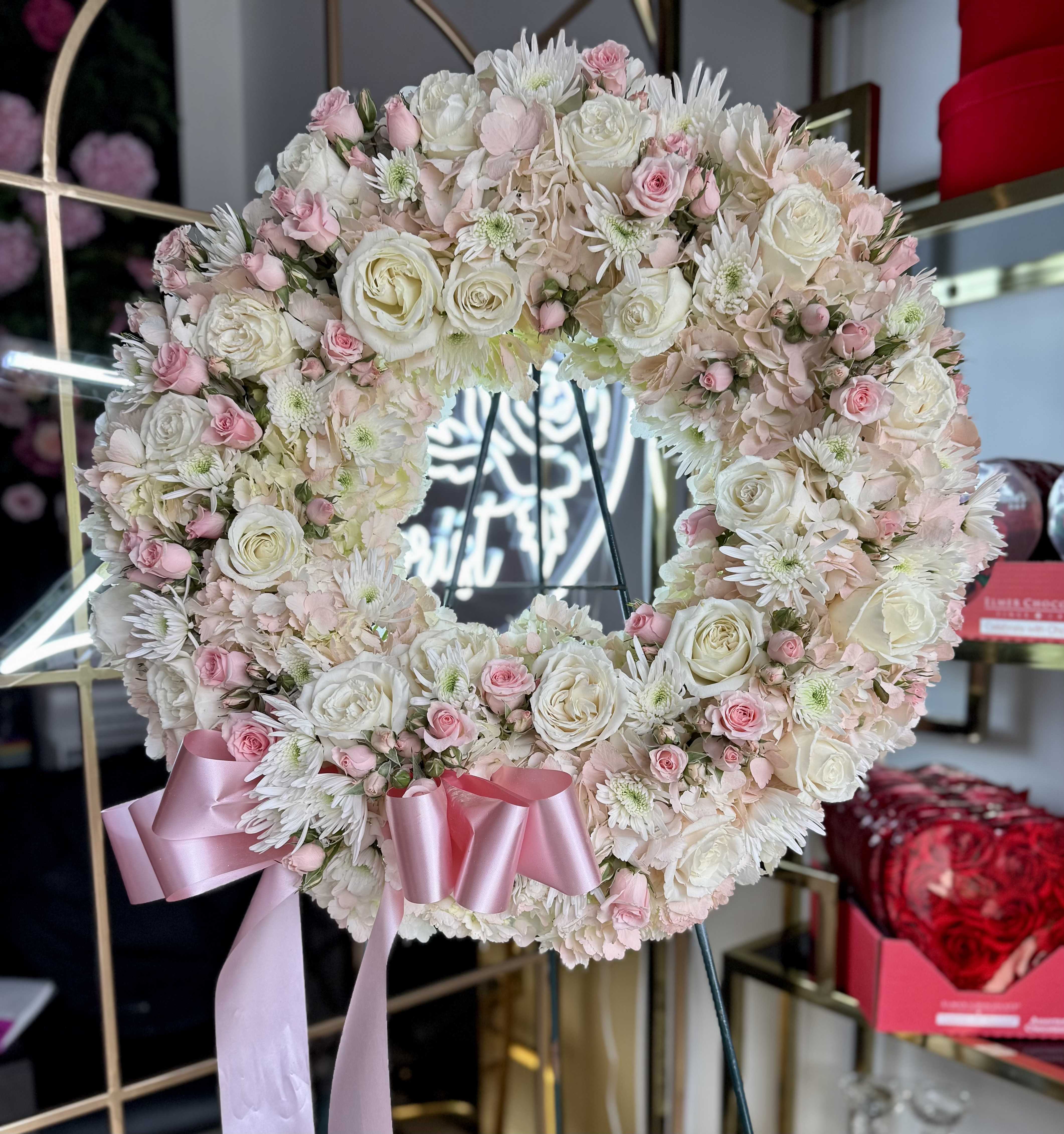 Pink &amp; White Sympathy Standing Spray - A beautiful tribute to a life remembered with love and grace. This round standing spray features a soft mix of pink and white blooms—such as roses, spray roses, carnations, daisy pompon, and mums—artfully arranged to create a gentle, comforting display. Presented on a standing easel, it offers heartfelt support and remembrance at funeral services, memorials, or graveside gatherings.  Custom flower selections and ribbon inscriptions available upon request. size approx 18&quot; 