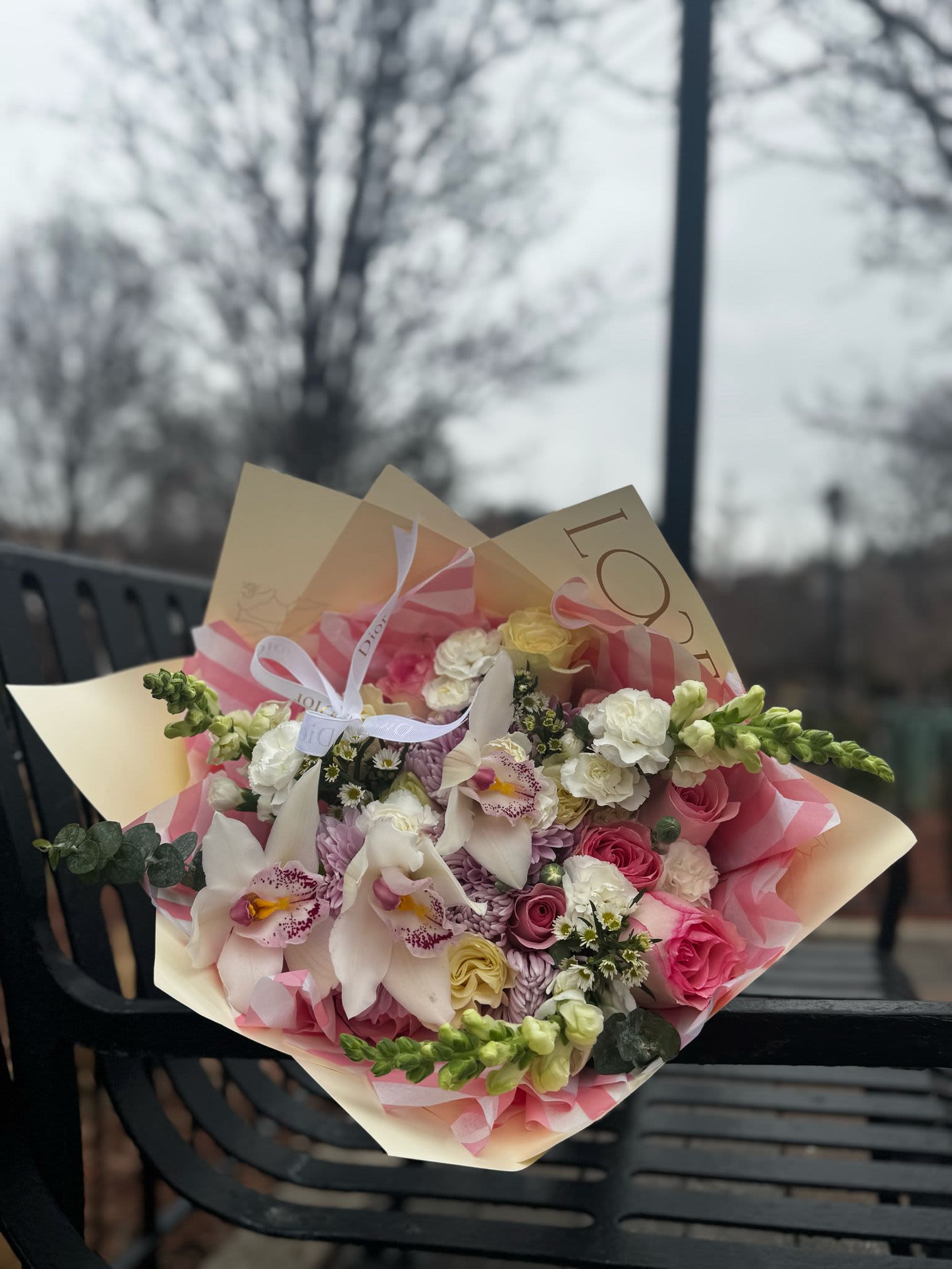 Armonia Primavera  - This bouquet is an exquisite floral arrangement with a harmonious combination of soft and delicate colors. It includes cymbidium orchids in cream tones with pink accents, roses in various shades of pink and pastel yellow, lilac chrysanthemums, mini white carnations, and a touch of green foliage that adds freshness and volume. It is wrapped in elegant beige and pink paper, with a ribbon bow that adds a sophisticated finish. Ideal for conveying tenderness, elegance, and admiration on any special occasion.