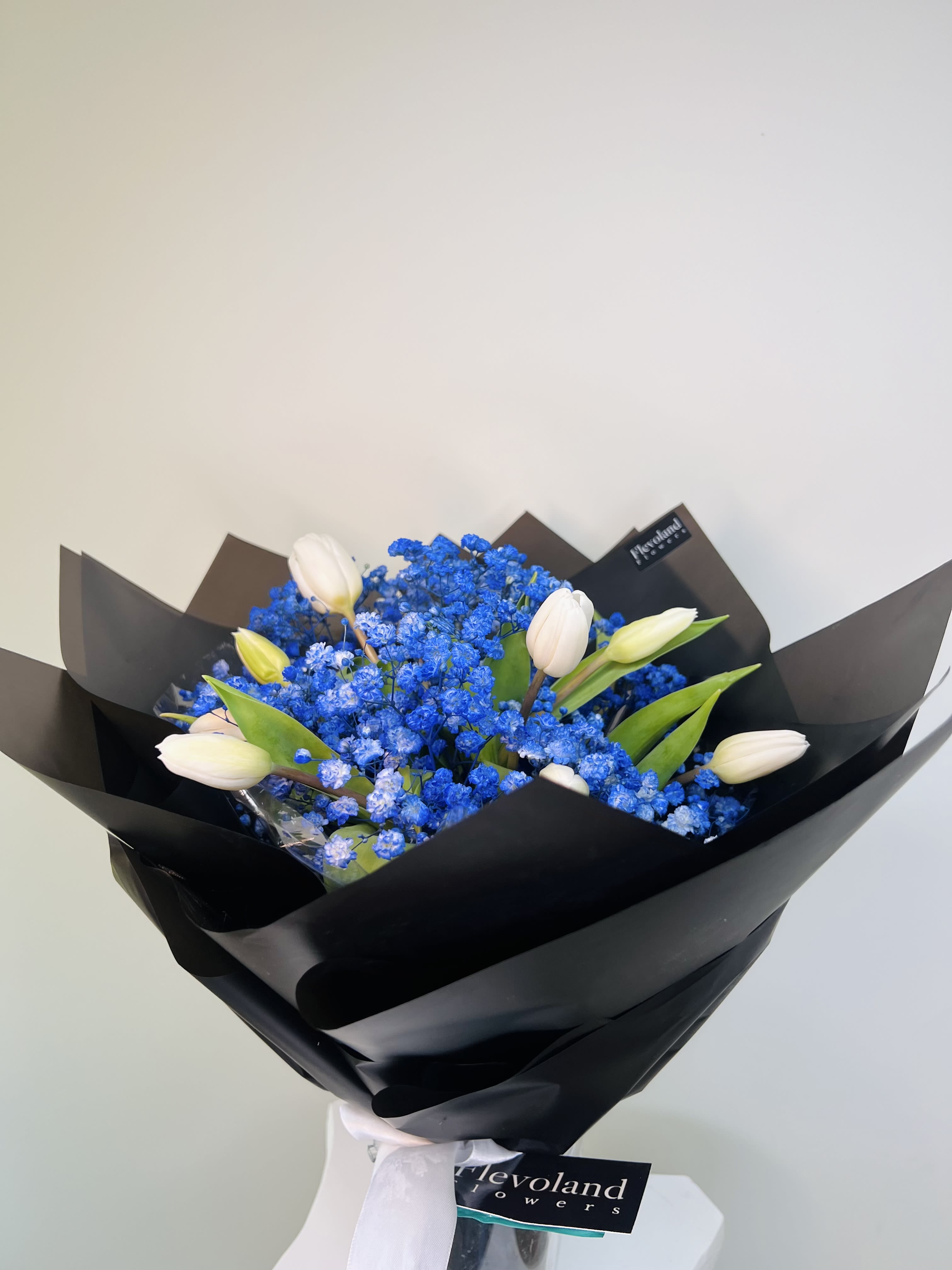 Deep Blue - White tulips paired with vivid blue baby’s breath, wrapped in matte black paper and tied with a white ribbon. A bold and elegant design perfect for a modern, masculine gesture with presence and style.
