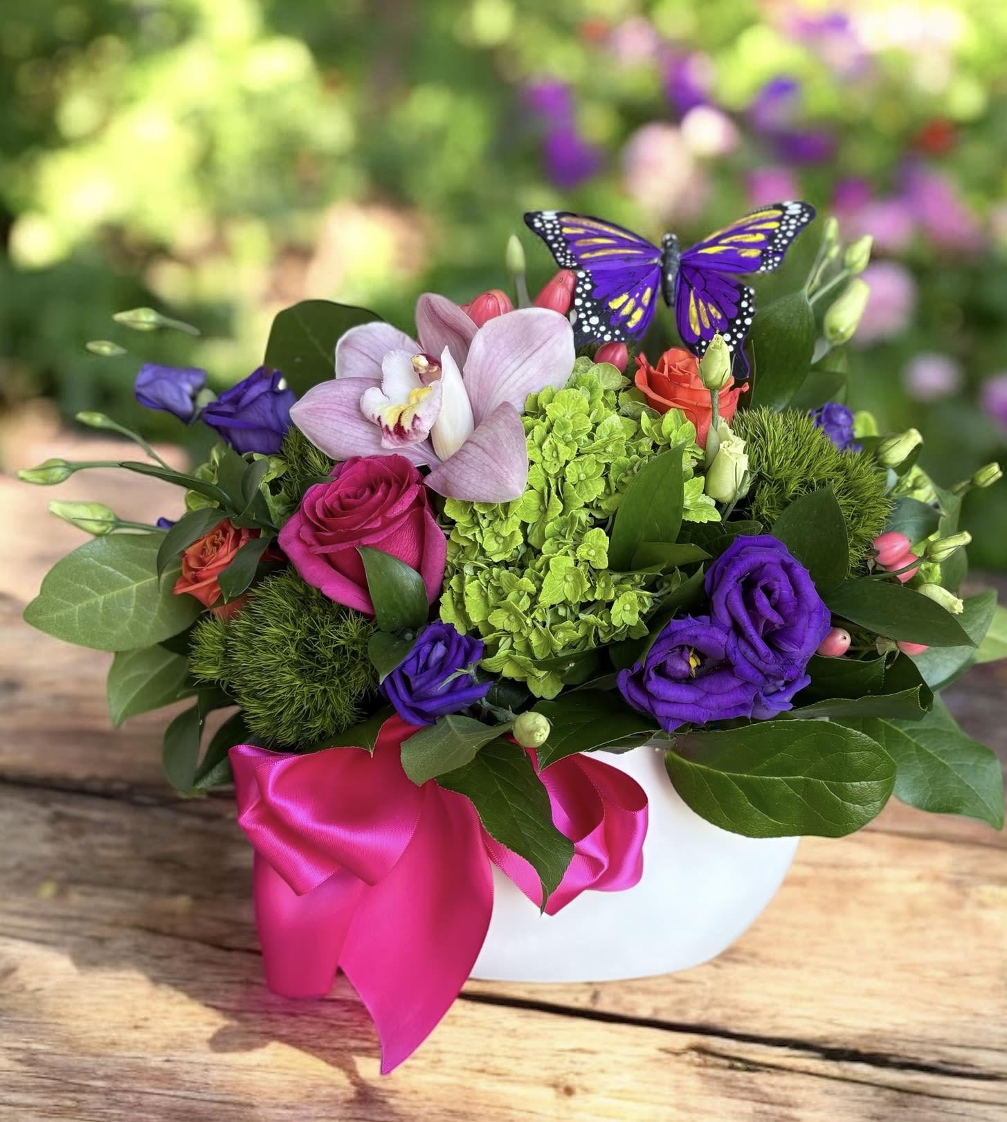 The Butterfly and Beyond The Butterfly and Beyond - The Butterfly and Beyond – Vibrant Mixed Floral Arrangement with Butterfly Accent | Wilmington, Delaware Local Florist Celebrate beauty and elegance with The Butterfly and Beyond, a stunning floral arrangement expertly crafted by your trusted Wilmington, Delaware florist. This vibrant bouquet features lush green hydrangea, fresh green trichilium, delicate purple lisianthus, bold dark pink roses, vivid hot pink roses, charming pink hypericum berries, and a graceful light pink orchid. A butterfly accent adds a whimsical touch, all beautifully arranged in a sleek white ceramic container and finished with a hot pink satin ribbon. Perfect for birthdays, anniversaries, congratulations, or just to brighten someone’s day. Available for same-day flower delivery in Wilmington, DE and nearby areas. Trust our local flower shop for premium blooms and personalized service.