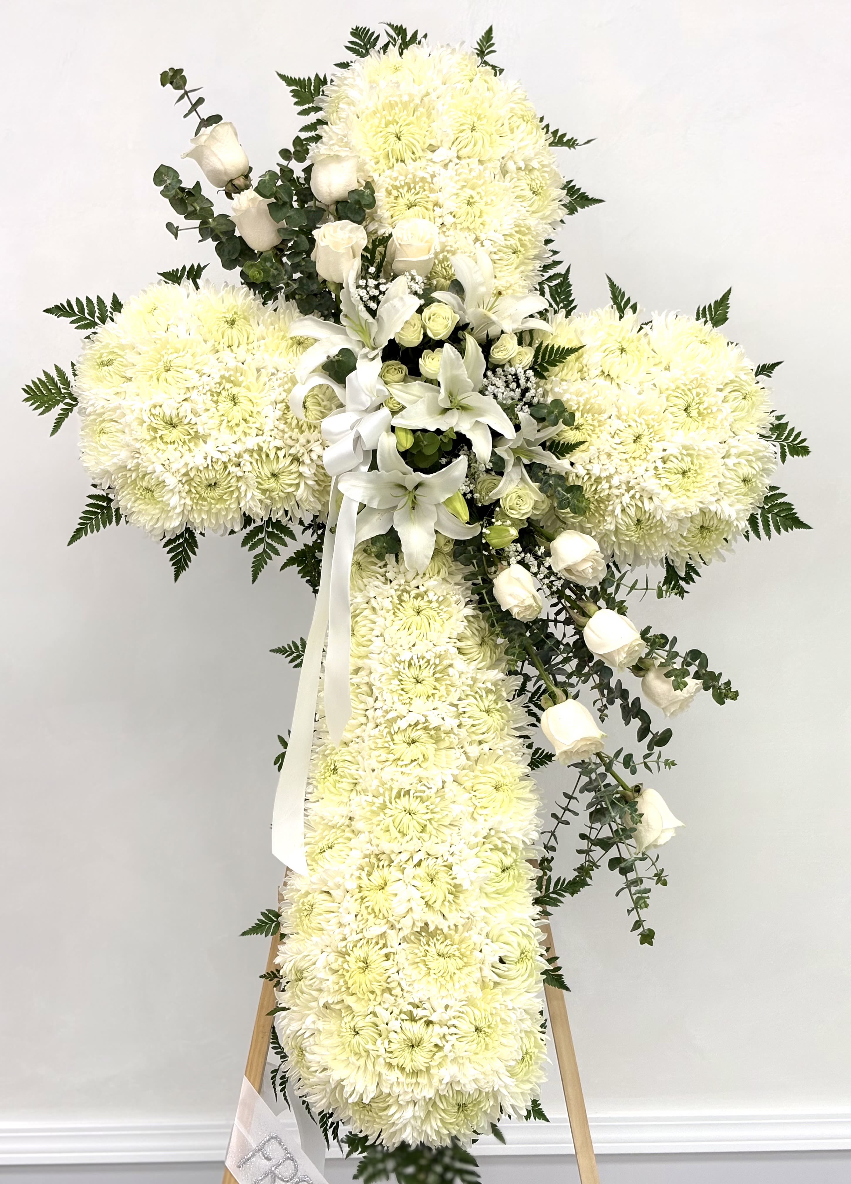 Eternal Grace Cross By VLM Flowers - A heartfelt tribute crafted in the shape of a cross, featuring pure white chrysanthemums and soft greenery. This elegant arrangement symbolizes peace, purity, and everlasting love, offering comfort and reverence in a time of remembrance.  We include easel, and delivery (some fees may apply).   Standard size is 30'', deluxe is 36'', and premium is 42''.