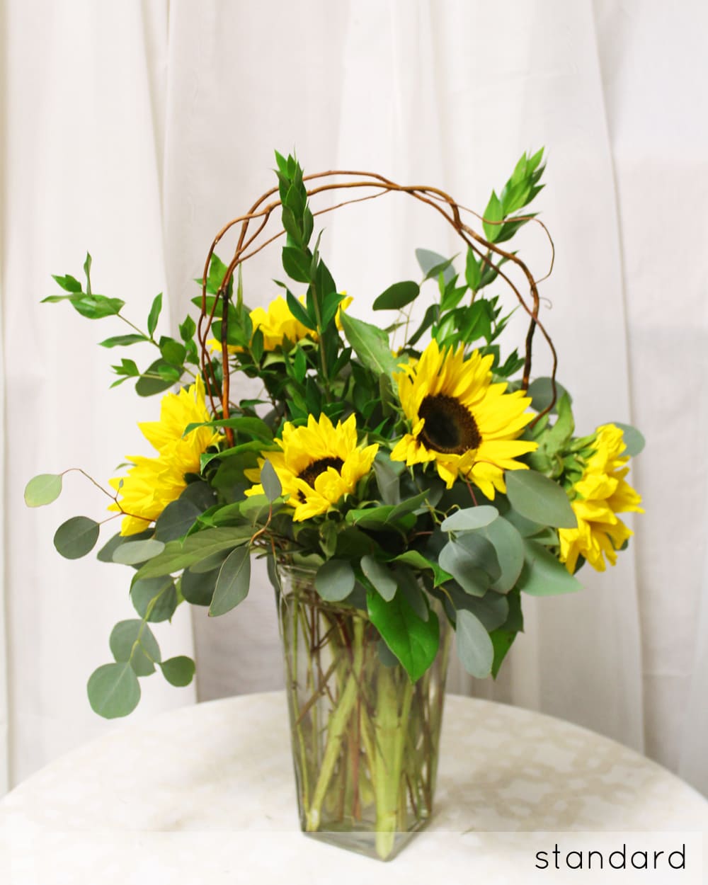 Sunflower Country - Bring a country feel into the home with this simple yet golden sunflower arrangement, accented with an rustic arch of willow branches.   Key notes for this design are sunflowers and curly willow. 
