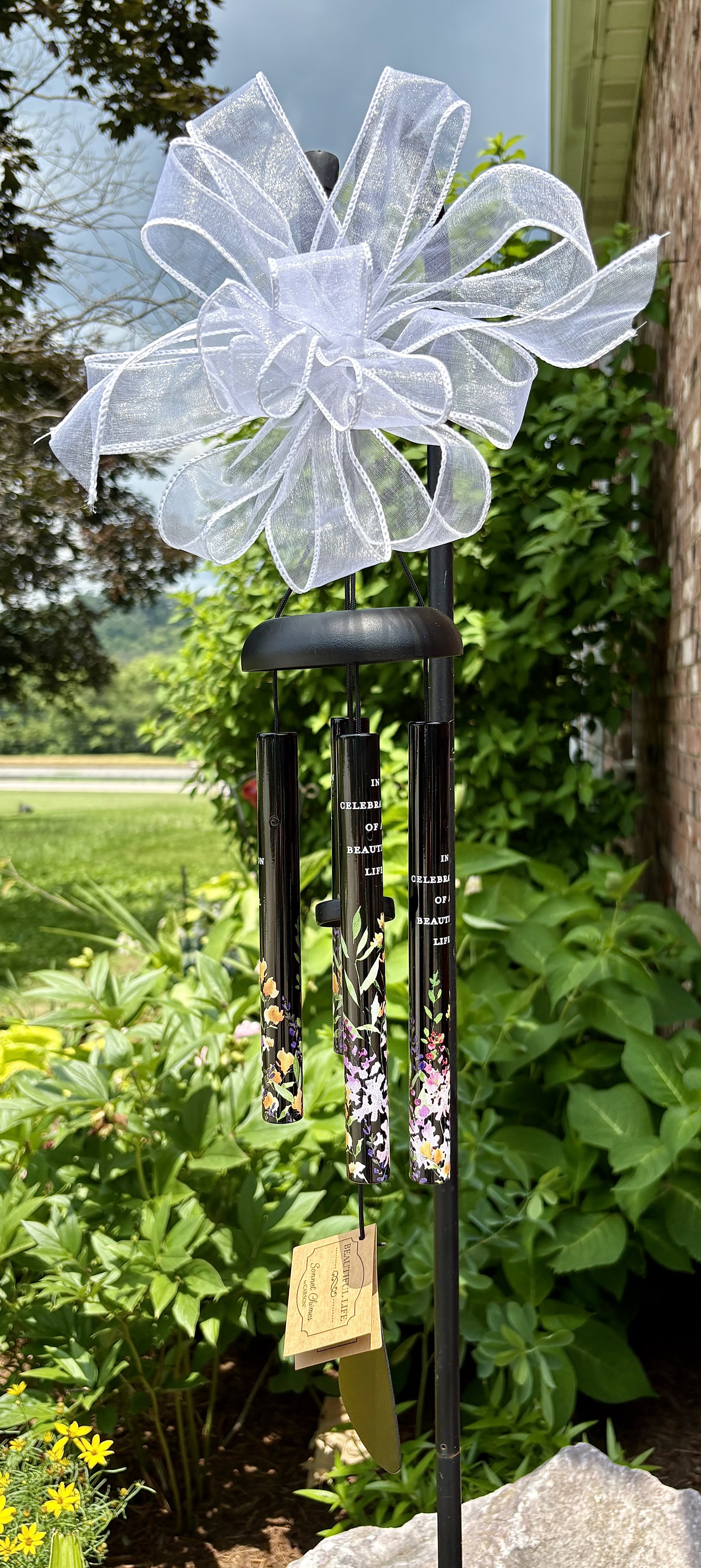 &quot;Beautiful Life&quot; 21&quot; Wind Chime - &quot;Beautiful Life &quot; 21&quot;  Wind In Memory” Sympathy Wind Chime  A Gentle Whisper of Love That Lasts Forever   Honor a cherished memory with our beautifully crafted “In Memory” Sympathy Wind Chime. Designed to bring comfort and peace, this elegant wind chime features five tuned aluminum tubes, each engraved with a heartfelt message of remembrance:  “Through the strongest of storms or softest breeze, listen to the wind and think of me.”  Accented with a delicate ivory lace top and a graceful white bow, this wind chime is not only a thoughtful tribute but also a serene addition to any garden, porch, or memorial space. The soft, melodic tones serve as a gentle reminder of the love that lives on.  Product Features: 	•	Material: Durable, weather-resistant aluminum and wood 	•	Finish: Brushed bronze with engraved text 	•	Length: Approximately 30 inches 	•	Includes: Memorial medallion with heartfelt verse 	•	Ready to Gift: Arrives adorned with a white decorative bow  Perfect for expressing sympathy, offering comfort, or remembering a loved one. 