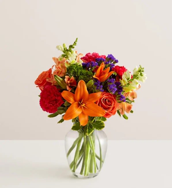 Harvest Heart - Through this colorful charming arrangement bring some more light into the life of your loved ones. Arrangement features orange lily. orange roses, red carnation, stock and other. 