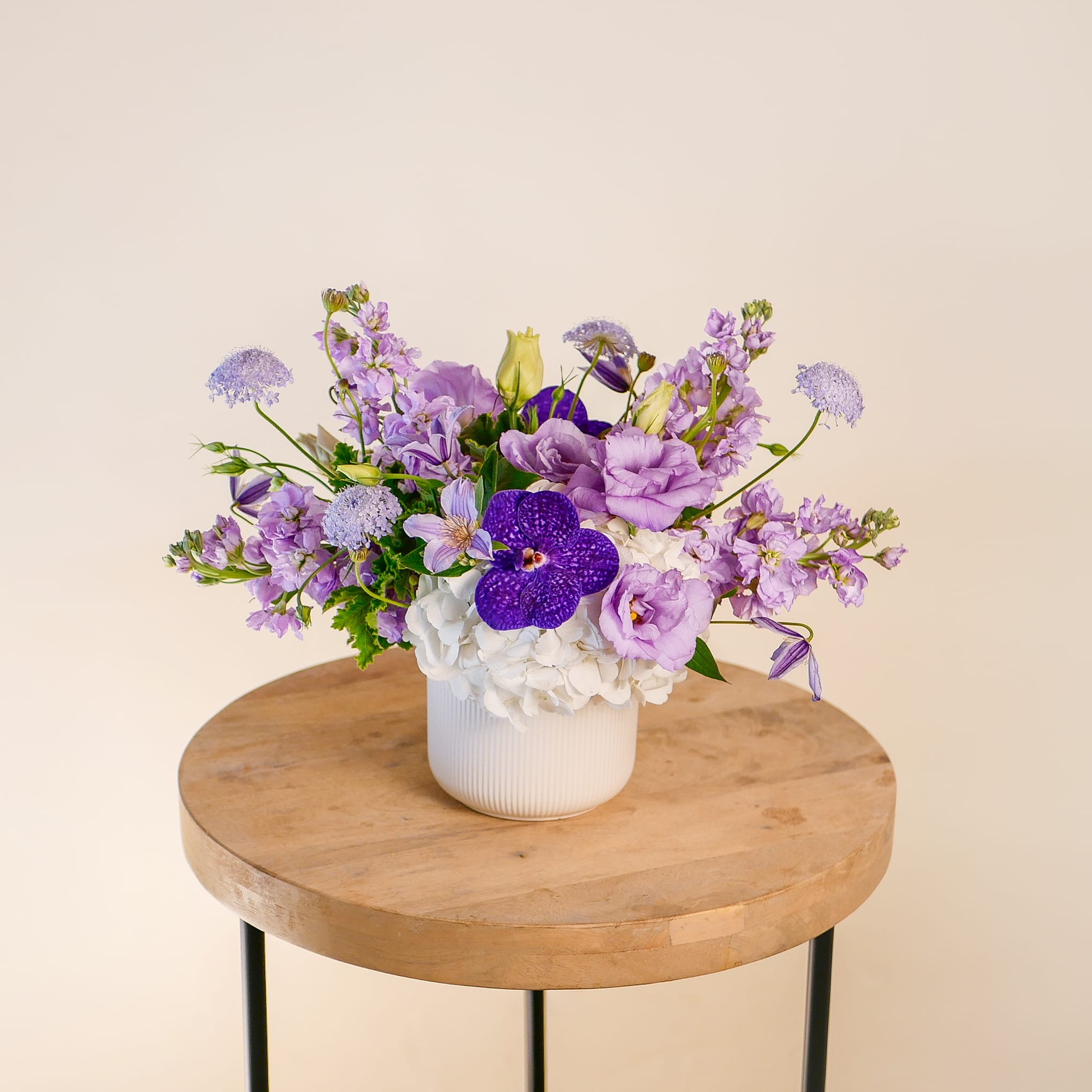 Lavender Haze - This enchanting monochromatic lavender arrangement showcases light purple lisianthus, clematis, fragrant stock, premium orchids, and white hydrangeas in a modern ceramic vase. It adds a touch of tranquility and sophistication, making it an ideal choice for special occasions or enhancing any space with its serene beauty. This arrangement approximately measures 11&quot; tall and 12&quot; wide with flowers.