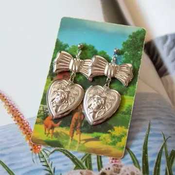 Vintage Bow & Heart Earrings Vintage Bow & Heart Earrings - Vintage pendant drop earrings with large silver bows and rose encapsulated in a heart. These are imitation rhodium - electroplated steel, with a bright silver look. They are lightweight and thin stampings. Made from deadstock vintage supplies and comes packaged on a vintage playing card (for a more sustainable option). All materials are secondhand & vintage to reduce our impact on the environment - some typical aging is to be expected but gives these pieces character. 1 3/4 inch overall length Bow is 1 inch wide Heart is 1 inch long x 7/8 inch wide