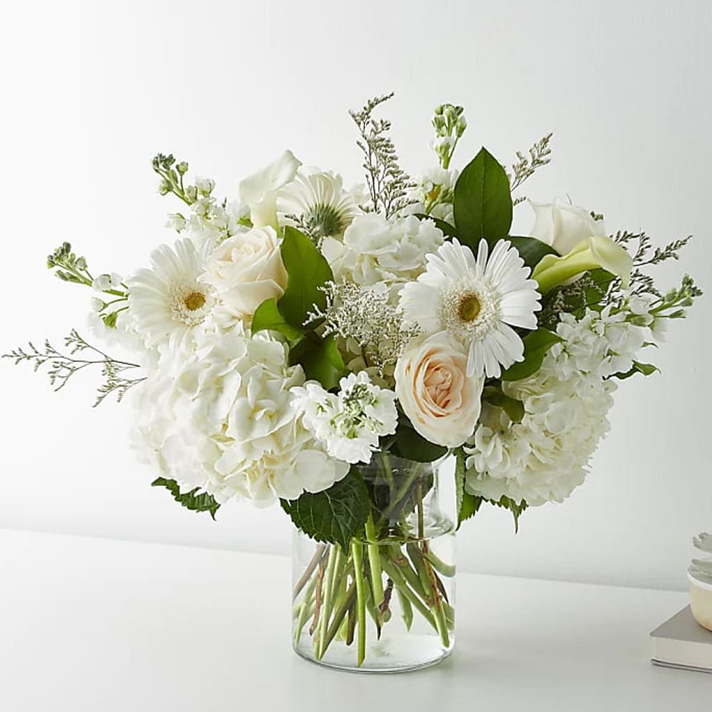 Vanilla Blossom Bouquet - Celebrate life's sweetest moments with our Vanilla Blossom Bouquet. A beautiful and classy arrangement hand-crafted with white roses, hydrangeas, gerbera daisies, mini calla lilies, and seasonal accents.  Delicate vanilla-colored blooms are arranged in a stunning bouquet, perfect for any occasion. Whether you're sending congratulations or expressing your love, this bouquet will surely delight.   Approximately 19&quot; H x 21&quot; W. 