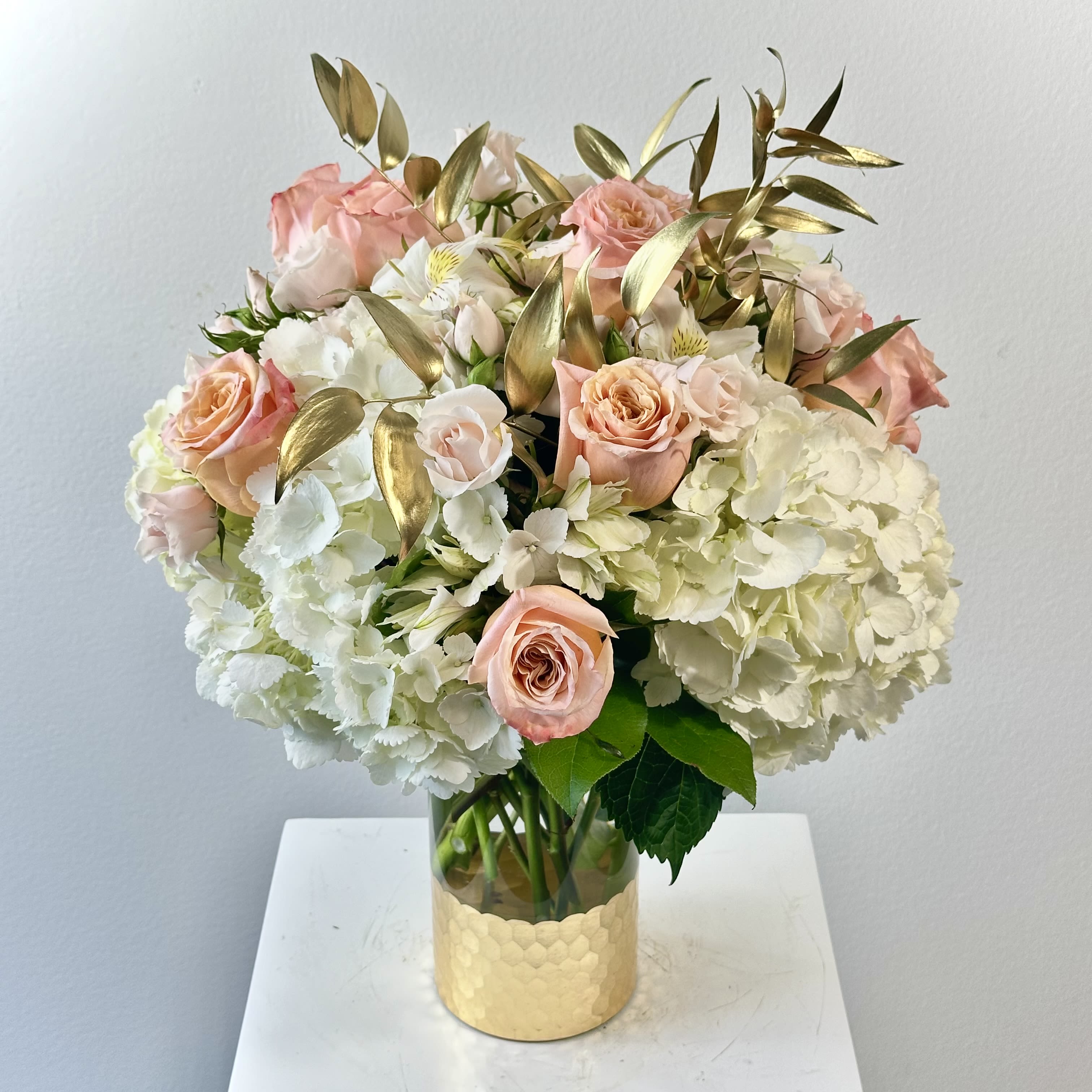 You Are Golden - You Are Golden: what expresses the intensity of a rose's personality, of love, of all things baroque? This mysterious, provocative and aristocratic design gradually reveals its contrasts to those who care to look more deeply within. White hydrangeas followed by light pink spray roses and are brought together with a beautiful peach roses. Subtly soft and beautiful. Main colors: white, peach. Typically includes: White Hydrangeas, waxflower, Peach Roses, Peach Spray Rose, Seeded Eucalyptus. Subject to substitution.