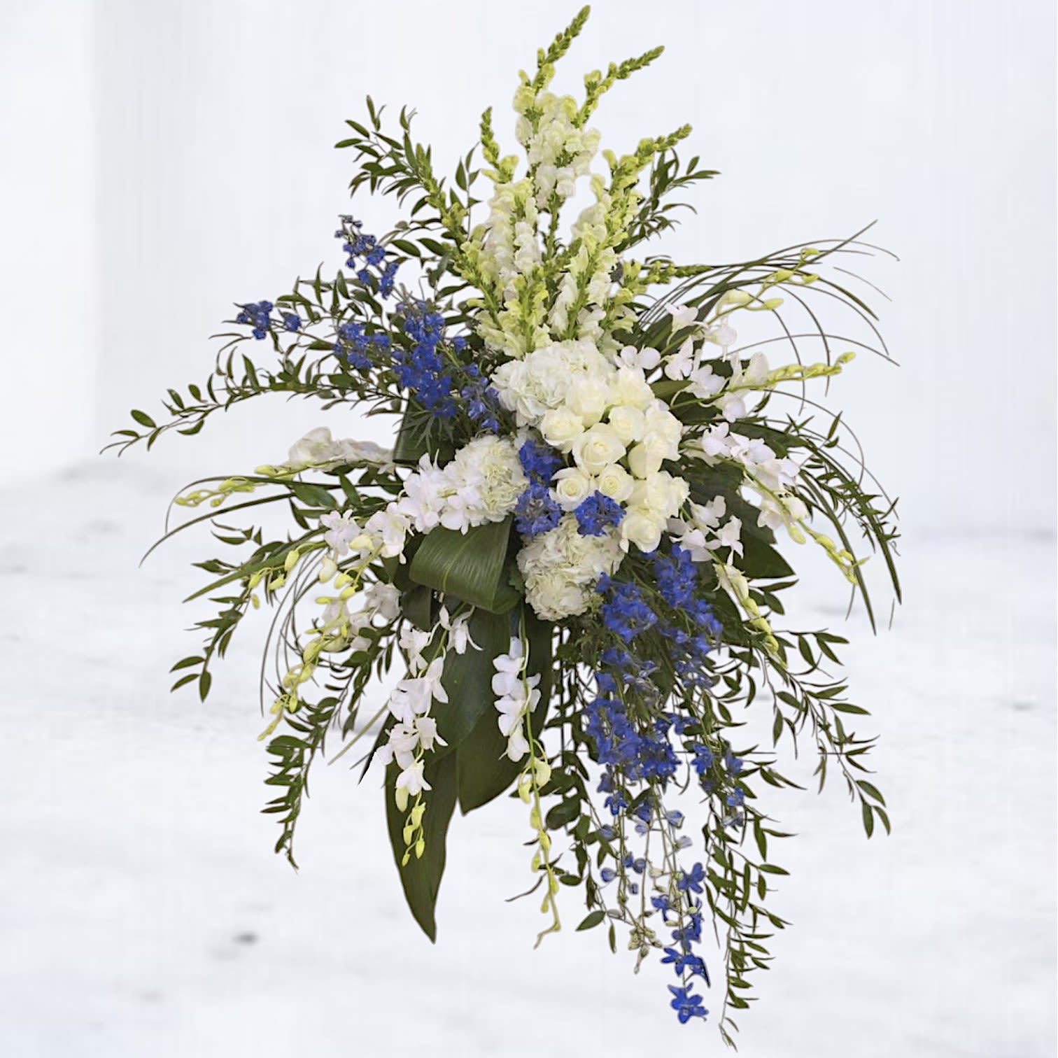 Tranquil Horizon Tribute Standing Spray Tranquil Horizon Tribute Standing Spray - Honor a loved one with the serene beauty of the Tranquil Horizon Tribute, a standing spray designed to evoke peace and grace. Featuring a harmonious blend of blue delphiniums, white dendrobium orchids, hydrangeas, and lush greenery, this arrangement captures the calming essence of the sky and sea. Perfect for memorials or funeral services, this design offers a meaningful way to express heartfelt condolences and celebrate a life well-lived. Easels are included with all standing sprays for effortless display at services.
