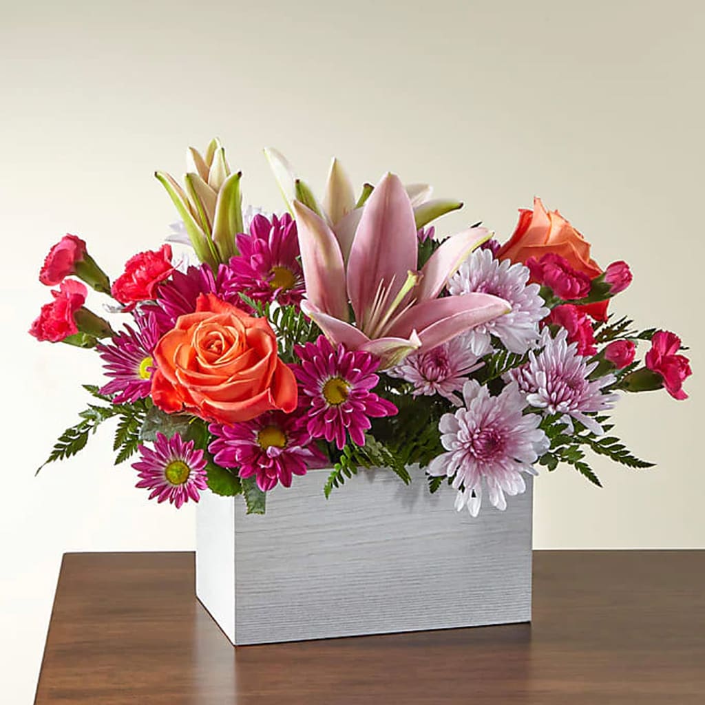 Light of My Life Box Bouquet - Brighten any day with this vibrant arrangement of hot pink carnations, orange roses, lavender cushion poms, and lush greens. A perfect way to celebrate your loved ones, no matter the occasion.  Approximate Size: 9&quot; H x 13&quot; W. Order now to send a burst of joy and color!