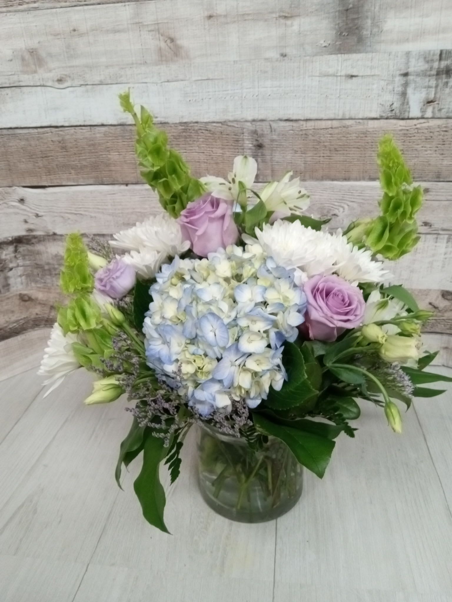 Coastal Breeze - Let the refreshing charm of the coast drift into your space with Coastal Breeze. This airy arrangement captures the essence of ocean-side serenity with soft blues, creamy whites, and subtle sandy hues. Featuring hydrangeas, delphinium, white roses, and textural greenery, it's designed to evoke salty sea air, sunlit shores, and gentle waves. Whether it’s a beachside celebration or a calming accent for your home, Coastal Breeze brings a breath of fresh air wherever it goes.