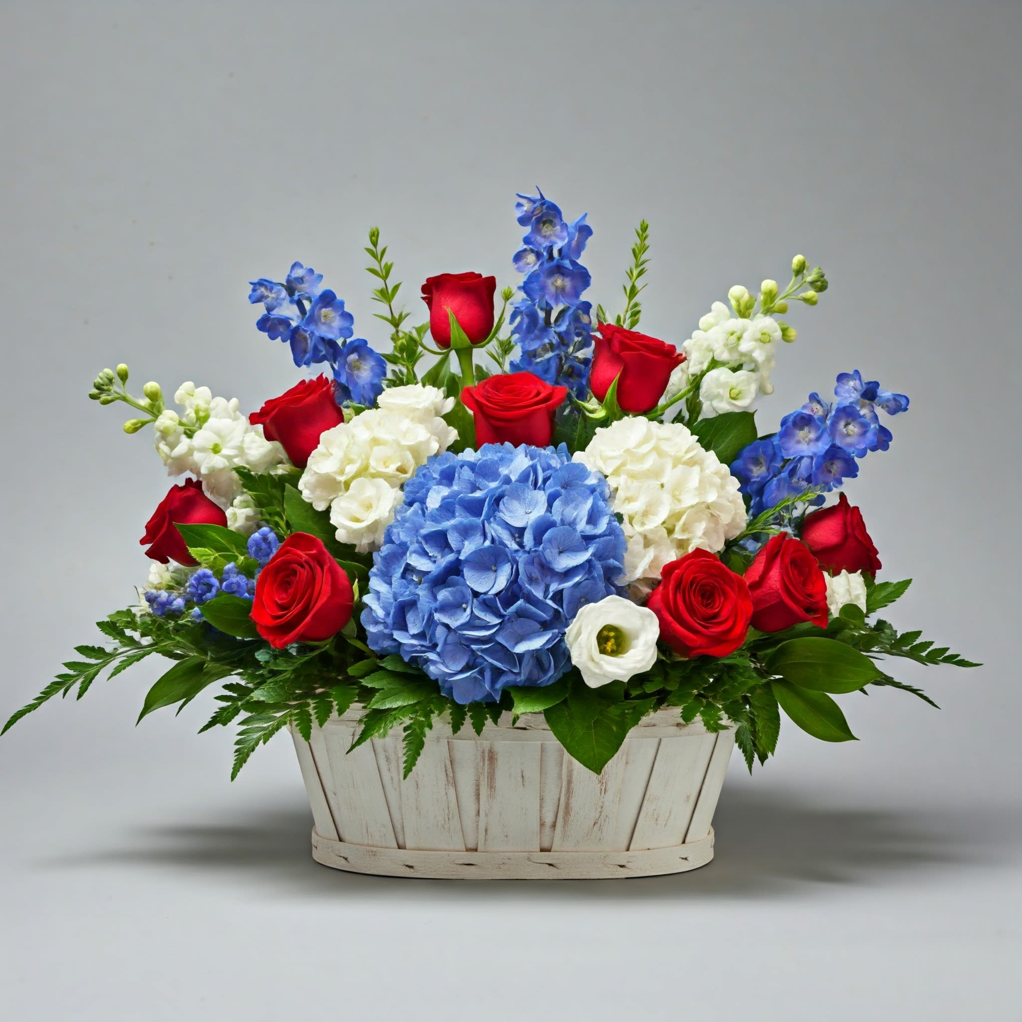 Forever America Basket Forever America Basket - A red, white, and blue basket featuring red roses, blue hydrangea, blue delphinium, and white stock.