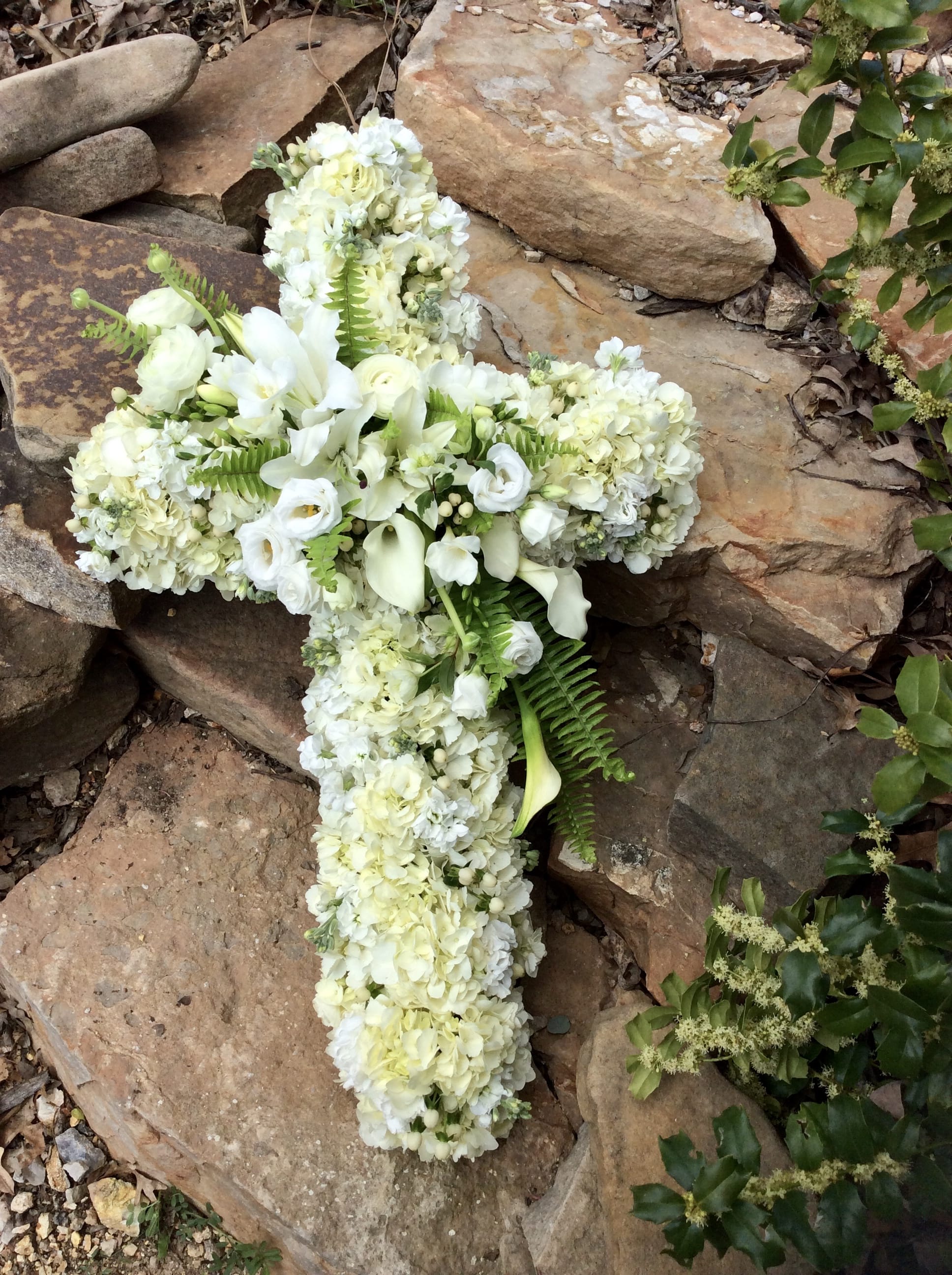 All Our Love  - Beautiful cross overflowing with white and green blooms. The arrangement is typically placed on an easel for an elegant display. Availability does vary. **Please call us to place an order.**