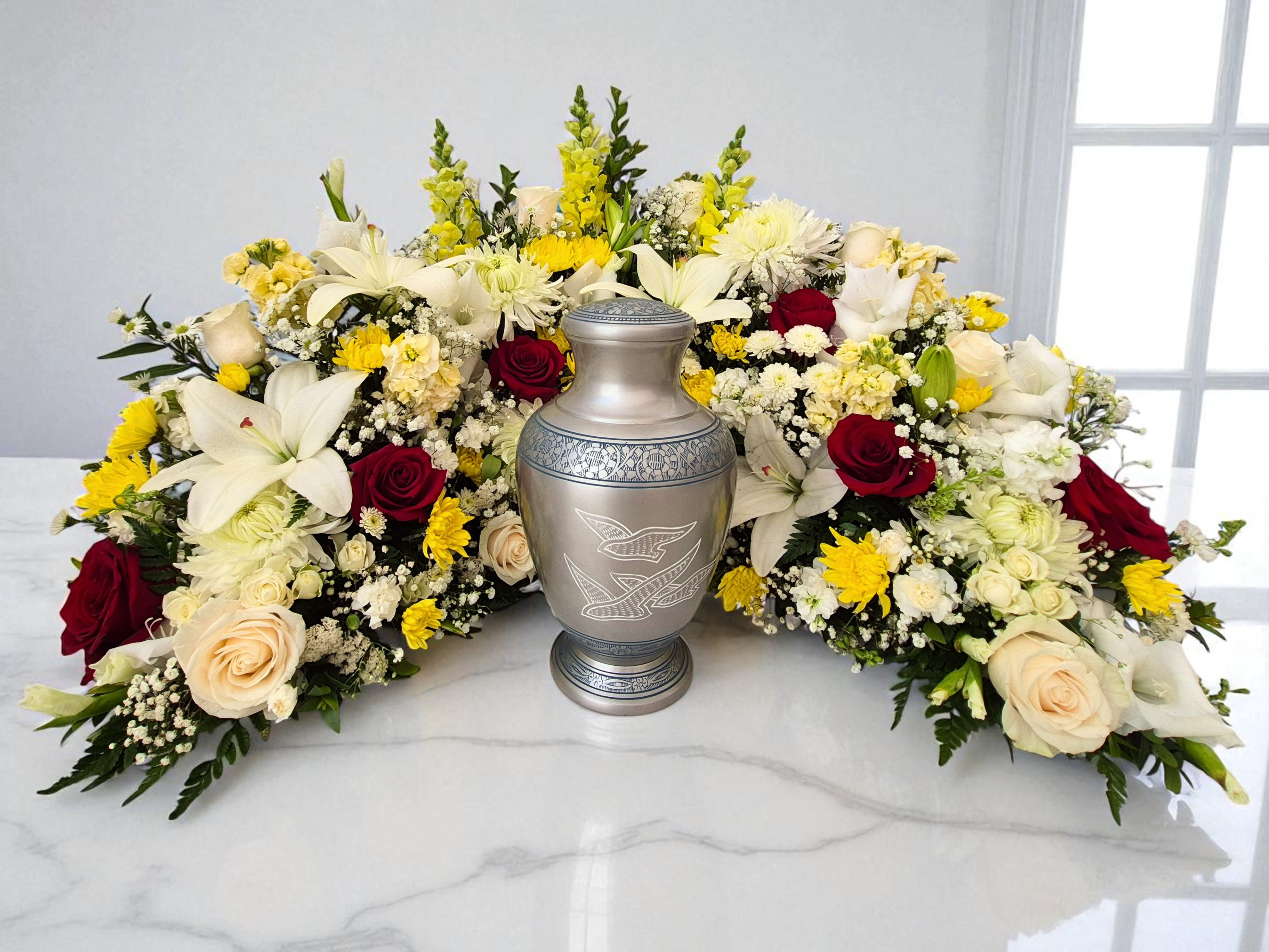 Celestial Embrace Urn Arrangement Celestial Embrace Urn Arrangement - This elegant floral tribute offers a tender and comforting display, perfect for a cremation funeral service. A graceful crescent moon, measuring approximately 20" tall, 34" long, and 20" wide, is meticulously crafted from a beautiful selection of roses, lilies, snapdragons, mums, and gladiolas, all accented by lush greenery. Designed to cradle a funeral urn at its center, this arrangement symbolizes eternal peace and enduring love, offering a serene focal point for remembrance. Flower colors can be customized to honor your loved one's memory; please specify your preferences in the special instructions or call us at 562-437-4106.