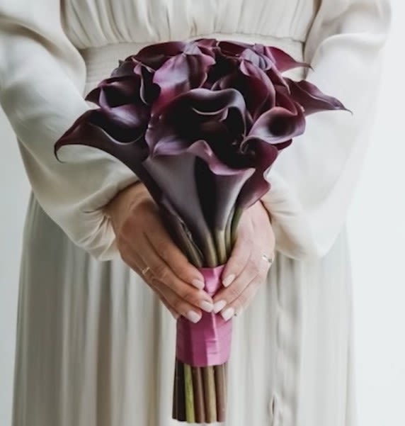 Midnight Elegance – Deep Calla Lily Bridal Bouquet - Bold, elegant, and unapologetically modern — this dramatic bridal bouquet features rich burgundy-black calla lilies, hand-tied with a deep satin ribbon for a clean, minimalist finish. The sculptural silhouette of the calla lilies brings effortless sophistication to any wedding look, especially for brides seeking a non-traditional or fashion-forward aesthetic.  The deep, velvety tones of the blooms evoke mystery, passion, and power, making this bouquet a striking statement piece for evening weddings, elopements, black-tie ceremonies, or modern city halls. Whether paired with a sleek gown or something romantic and flowing, this bouquet adds bold contrast and unforgettable beauty.  Perfect for the confident, artistic, and stylish bride, this bouquet is both timeless and unexpected — a true reflection of personal style.  Same-day wedding flower delivery available in Los Angeles.