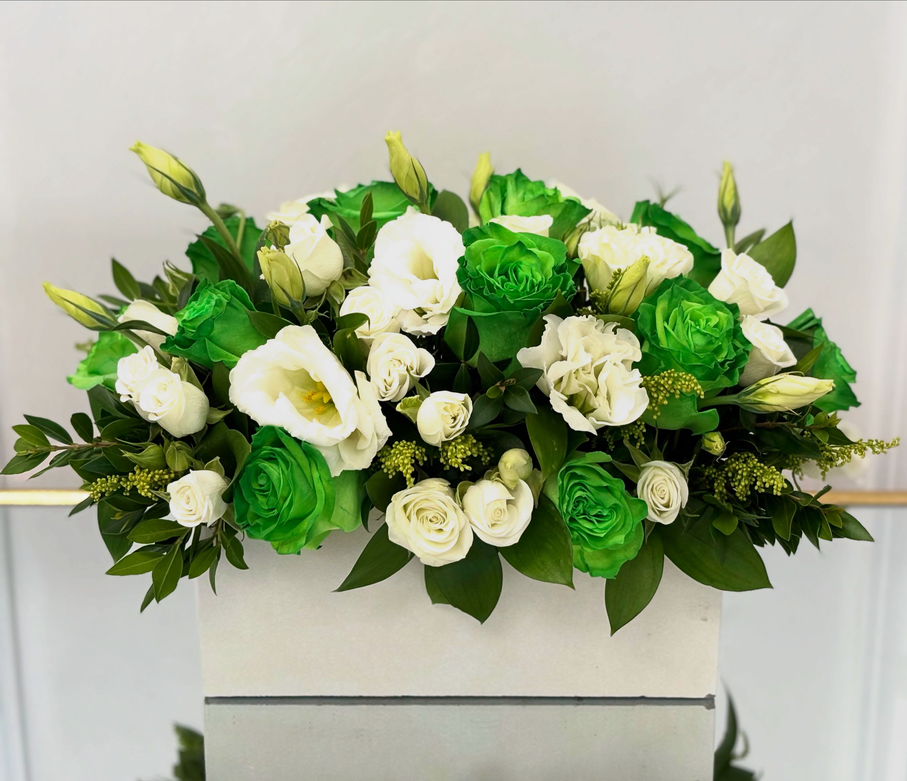 Verdant Grace By VLM Flowers - A striking expression of balance and renewal, Verdant Grace showcases a lush blend of emerald-green and creamy white roses, accented by lisianthus, spray roses, and fresh foliage. Set in a modern white vase, this arrangement feels both contemporary and symbolic — ideal for celebrating new beginnings, sending wishes of good health, or making a bold statement of elegance. A refreshing alternative to traditional floral palettes.