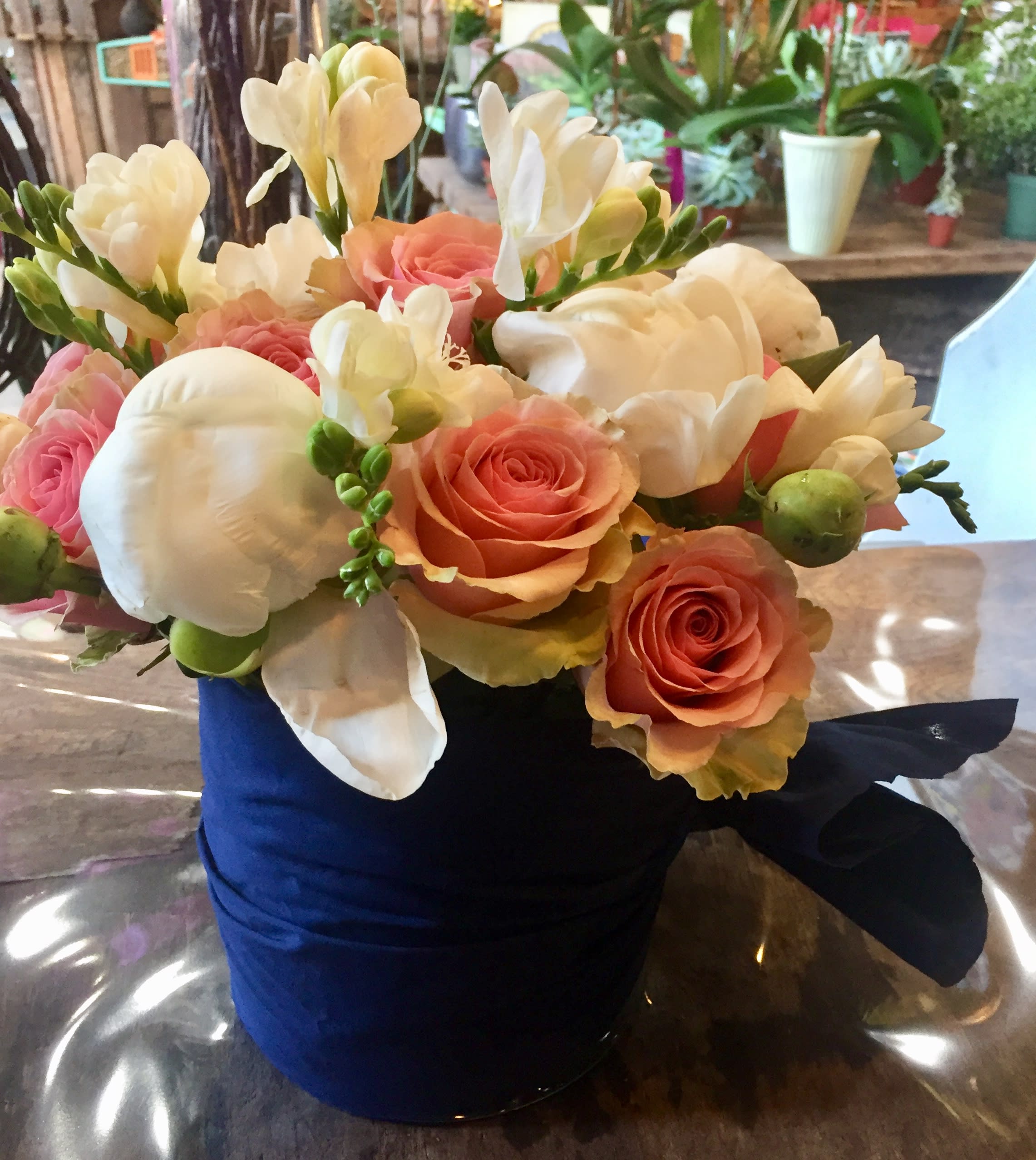 In The Navy - Fresh cut white freesia, white peony ONLY IF IN SEASON, FRESH AND AVAILABLE and pink garden roses fill this low profile cylinder or square vase wrapped in a navy cotton swag