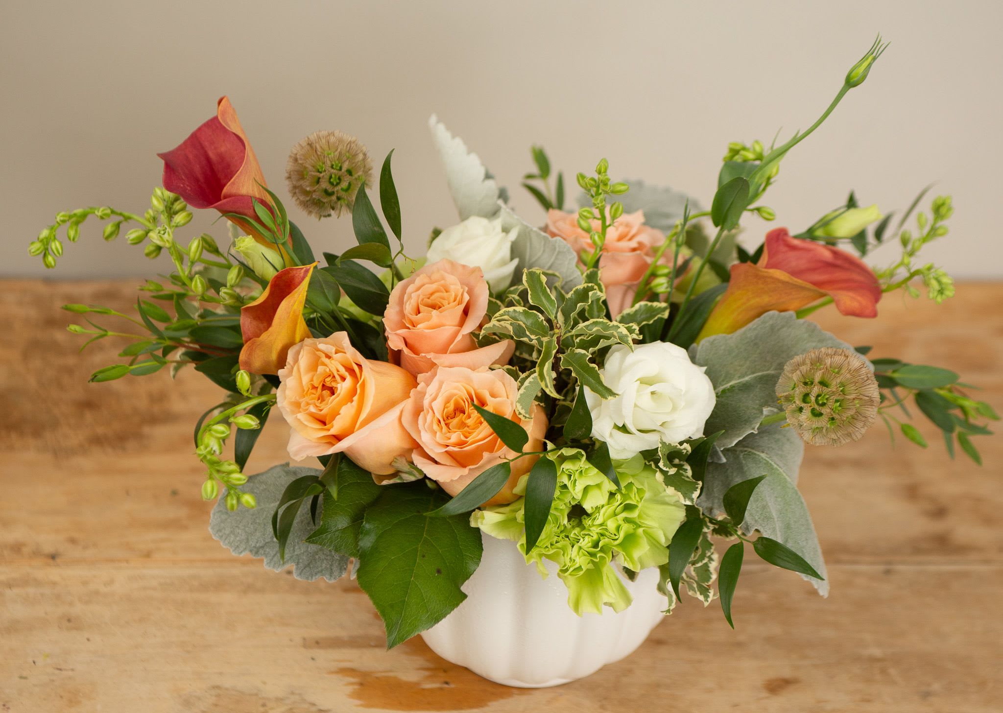 Sunkissed Grove - Inspired by the golden tones of late summer, this artful arrangement blends apricot roses, bronze calla lilies, creamy whites, and bright green ruffled blooms, all nestled in soft, silvery foliage. With its natural shape and sun-warmed palette, Sunkissed Grove feels like a stroll through a blooming orchard at golden hour—earthy, elegant, and effortlessly summery.
