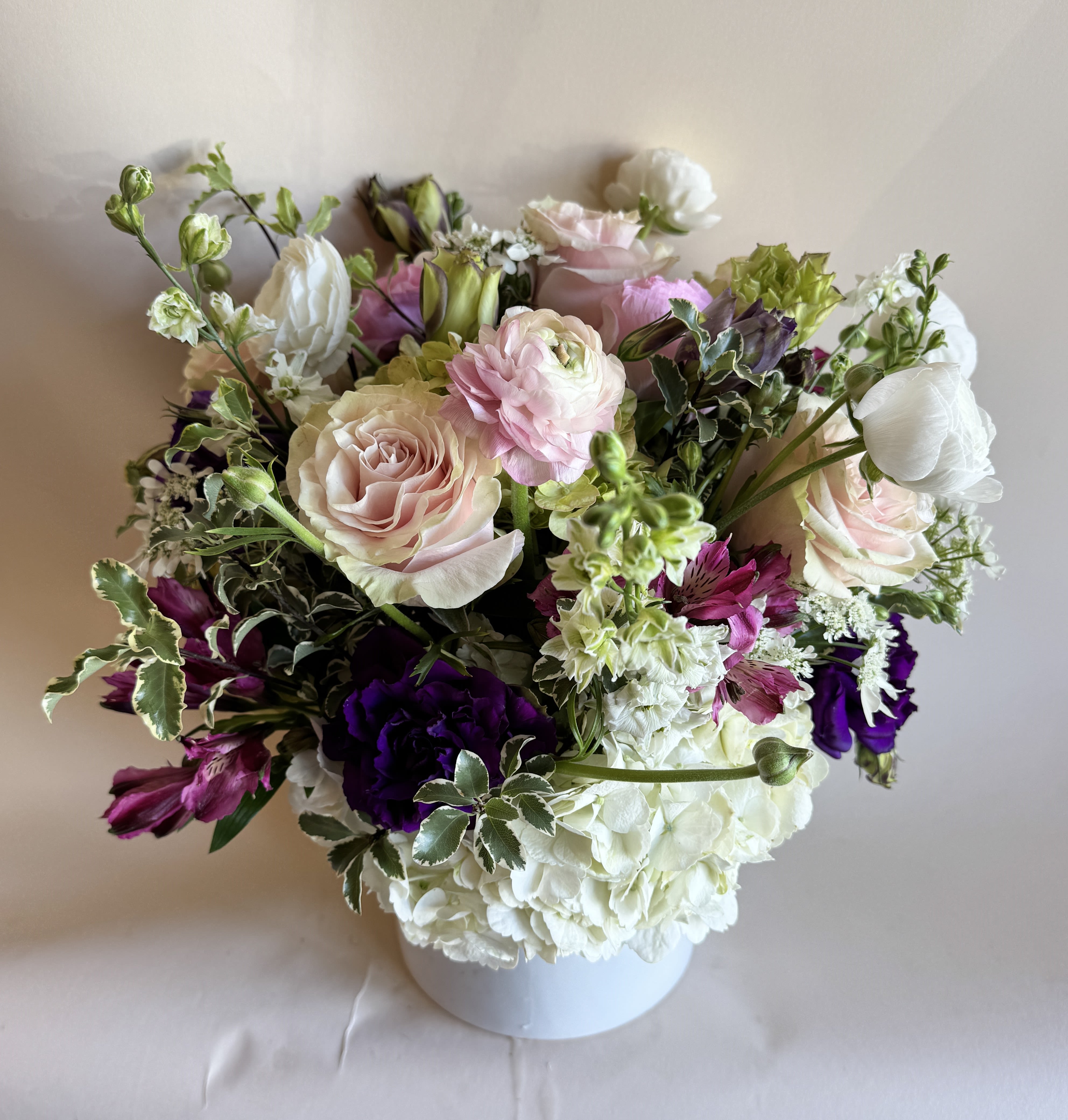 Soft Garden - A romantic and elegant floral arrangement bursts with soft, complementary hues of purple, pink, and white. Arrangement includes roses, orchids, hydrangeas, and other seasonal flowers. 