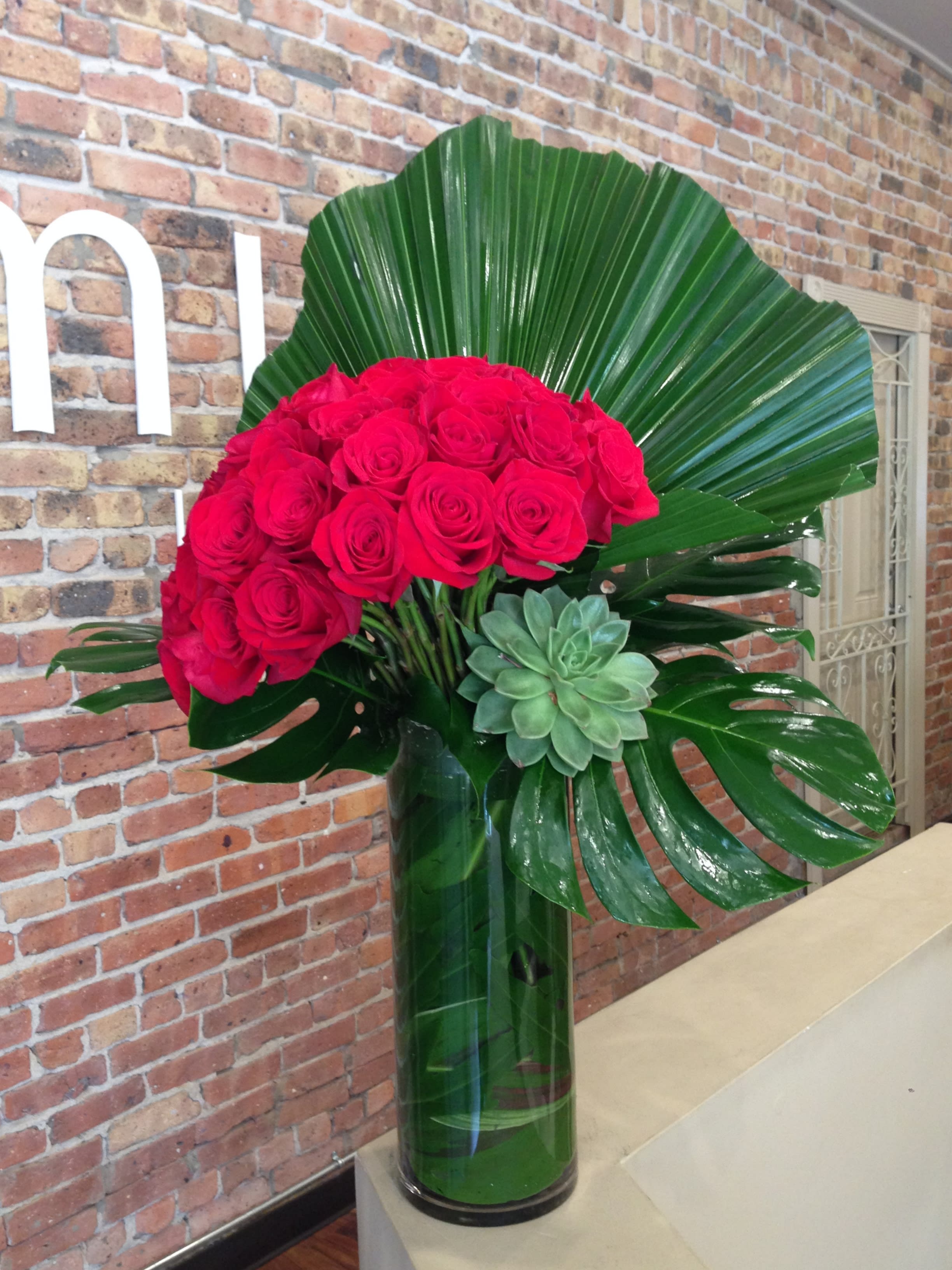 50 Premium Rich Red Roses 50 Premium Rich Red Roses - A leaning bouquet of 50 premium, long stemmed red roses create a show stopping arrangement with large tropical foliage and a succulent in a tall, sleek cylinder. Vase size 20" tall x 6" wide PLUS the flowers.