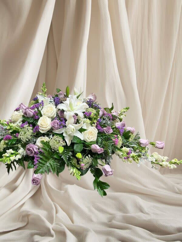 Lavender/White Casket Spray/ 5 -7 Days - A flourishing beautiful spray of soft beautiful lavender and white roses, white lilies, and a variety of other lavender, white, and green flowers and foliage.  Please allow 5–7 business days for all sympathy arrangements to ensure they arrive with care and consideration. Orders without a proper delivery date will be canceled.   Please contact the shop for further details