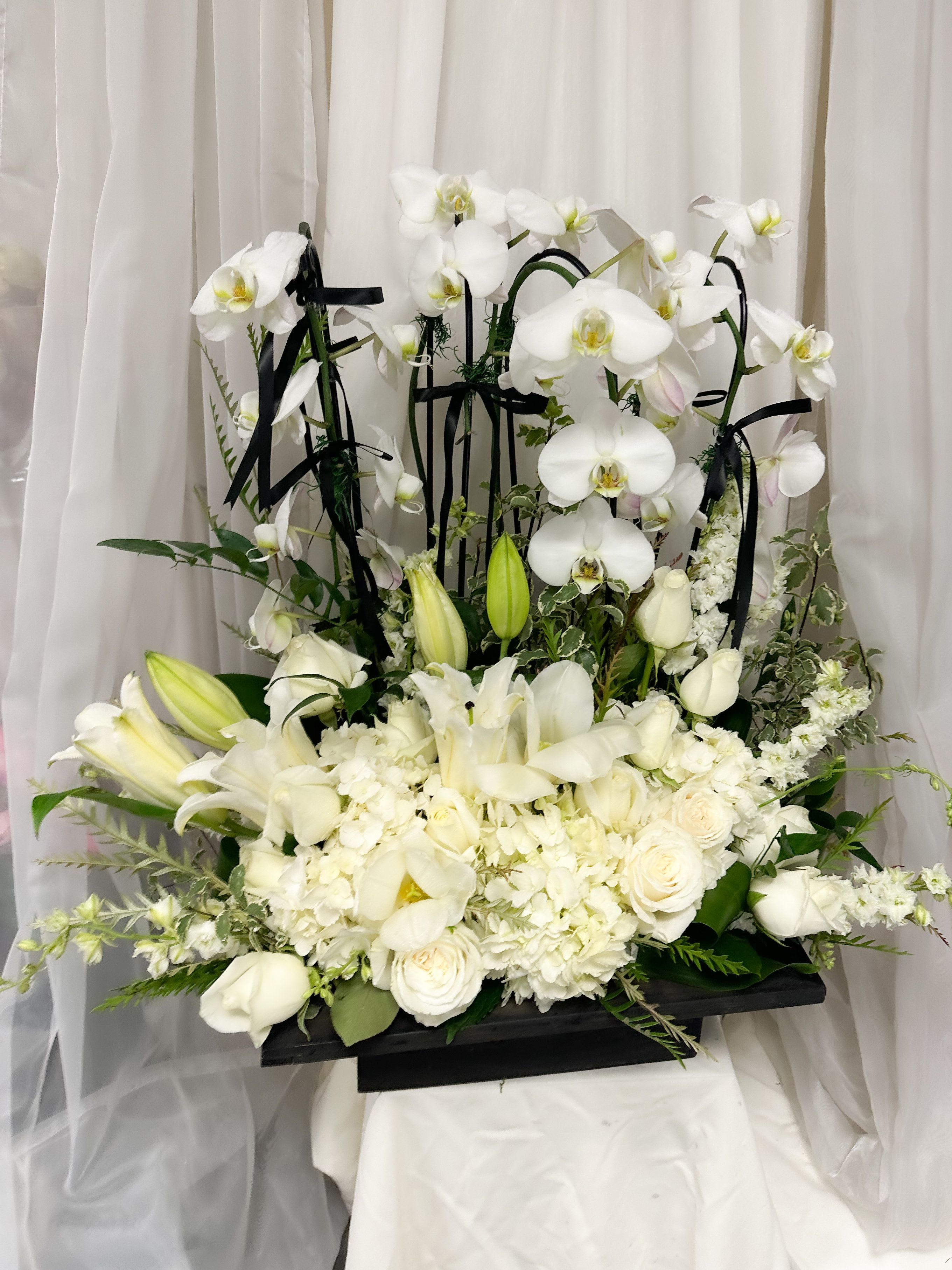 Eternal Orchid Grace - A breathtaking blend of timeless beauty and refined elegance, Eternal Grace is our signature orchid arrangement designed to leave a lasting impression. Featuring pristine phalaenopsis orchid stems paired with premium seasonal blooms like roses, white ranunculus, lilies, and hydrangeas—this arrangement is a harmonious balance of softness and sophistication.  Expertly arranged in a modern container, Eternal Grace is ideal for anniversaries, sympathy gestures, milestone celebrations, or simply to elevate your space with natural luxury.   Features:    •   2-3 premium phalaenopsis orchid stems    •   Hand-selected seasonal blooms in neutral and blush tones    •   Luxe designer container included    •   Available in standard, deluxe, and premium sizes    •   Custom color options upon request