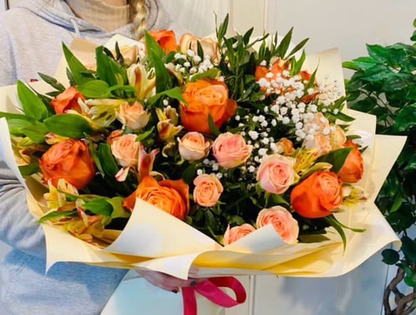 Bouquet with Orange Roses - Delight in the elegance of this bouquet featuring vibrant orange roses, tender spray roses in soft peach, and delicate alstroemeria blooms, accented by airy baby's breath and lush greenery. Wrapped in a light pastel ribbon, this arrangement exudes warmth and charm, perfect for any heartfelt occasion!