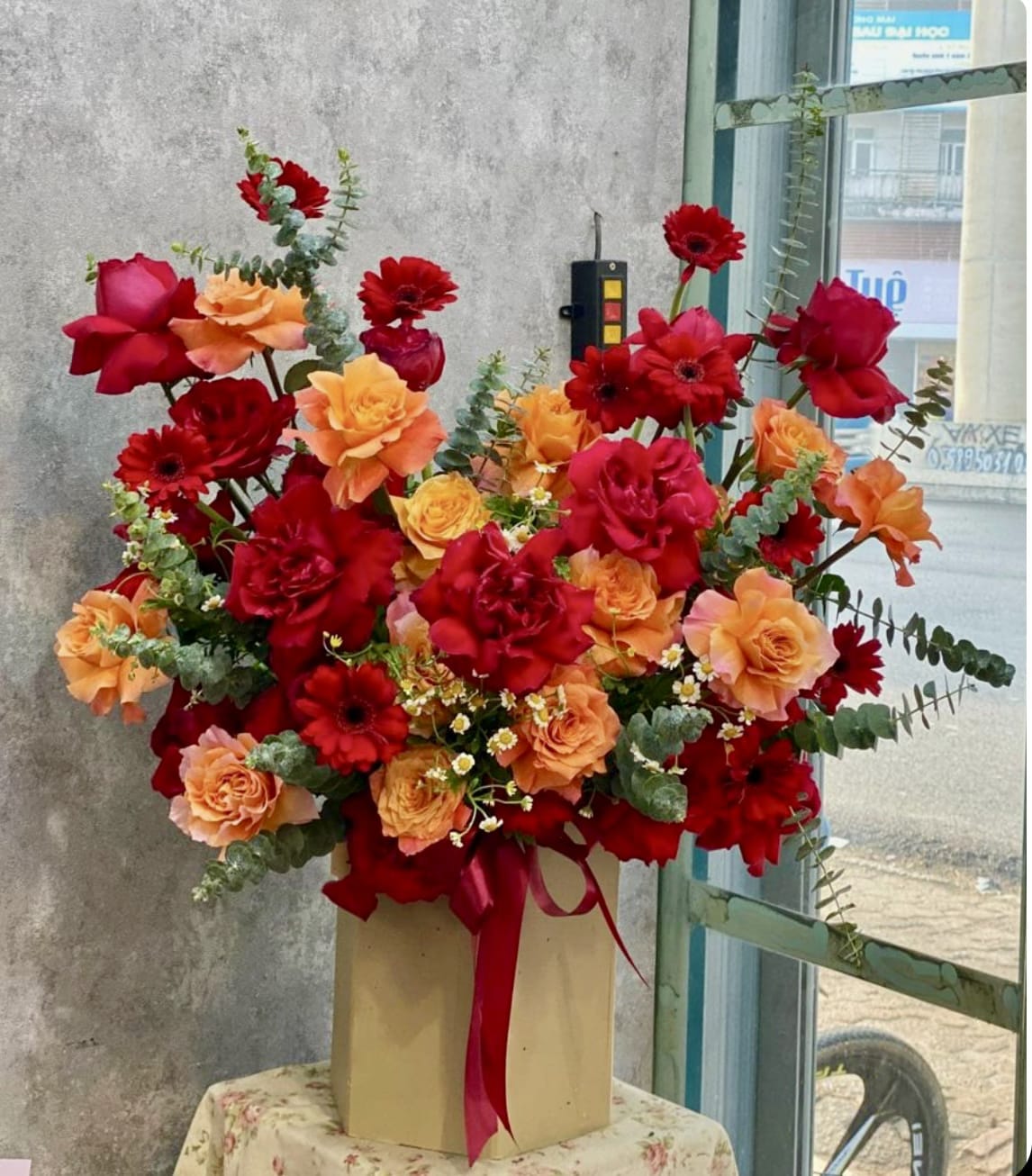Red &amp; Orange Roses - Express your deepest emotions with this heart-shaped arrangement of radiant red and warm orange roses, paired with elegant red gerberas and delicate chamomile blooms. Accented by lush eucalyptus and finished with a flowing crimson ribbon, this bouquet is a perfect symbol of love and passion.