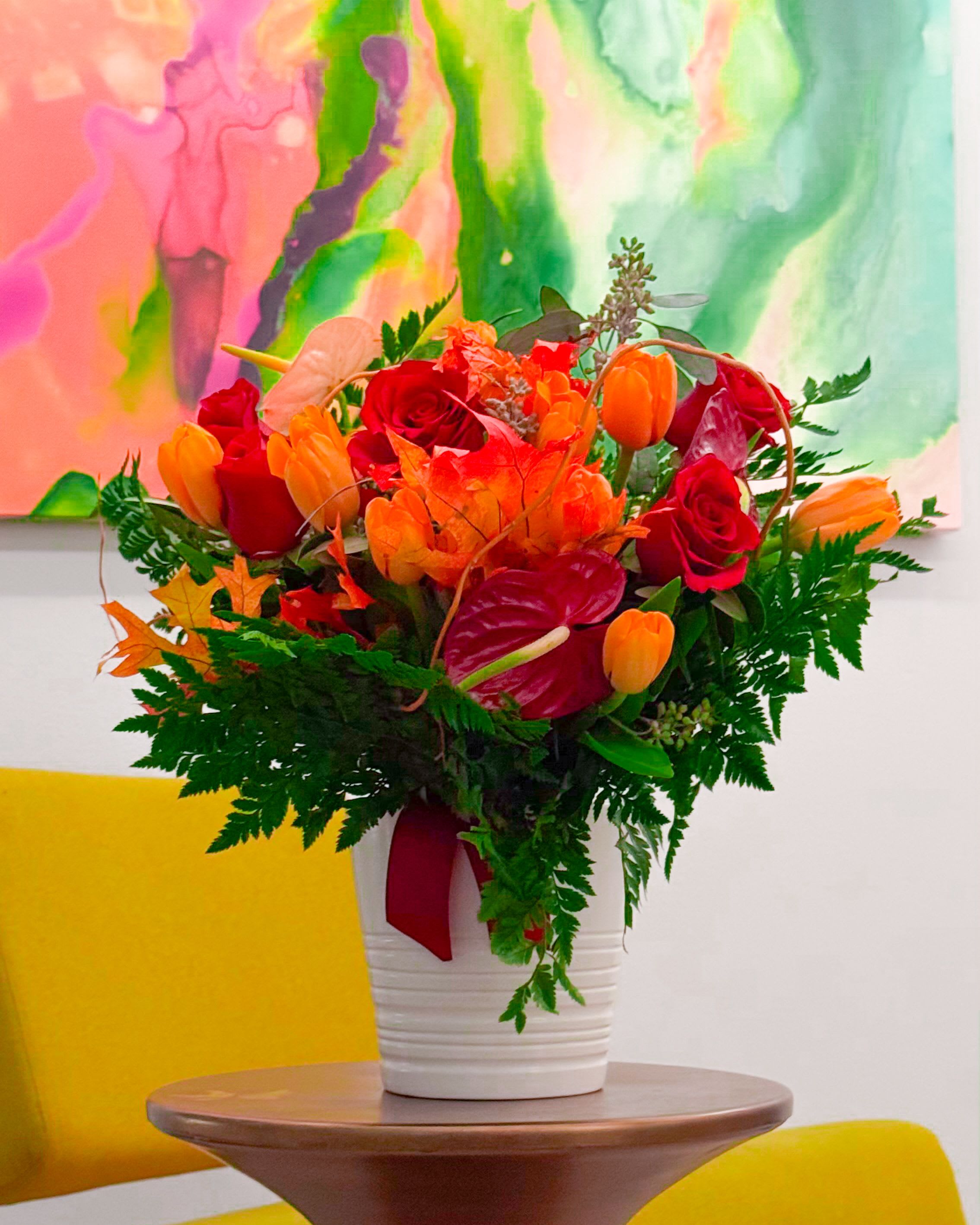 Fall Sunset - The “Fall Sunset” bouquet captures the vibrant beauty of autumn with red roses, orange tulips, exotic anthuriums, and seasonal maple leaves, all complemented by lush greenery. Perfect for any occasion, this fiery arrangement brings warmth and charm to your space.
