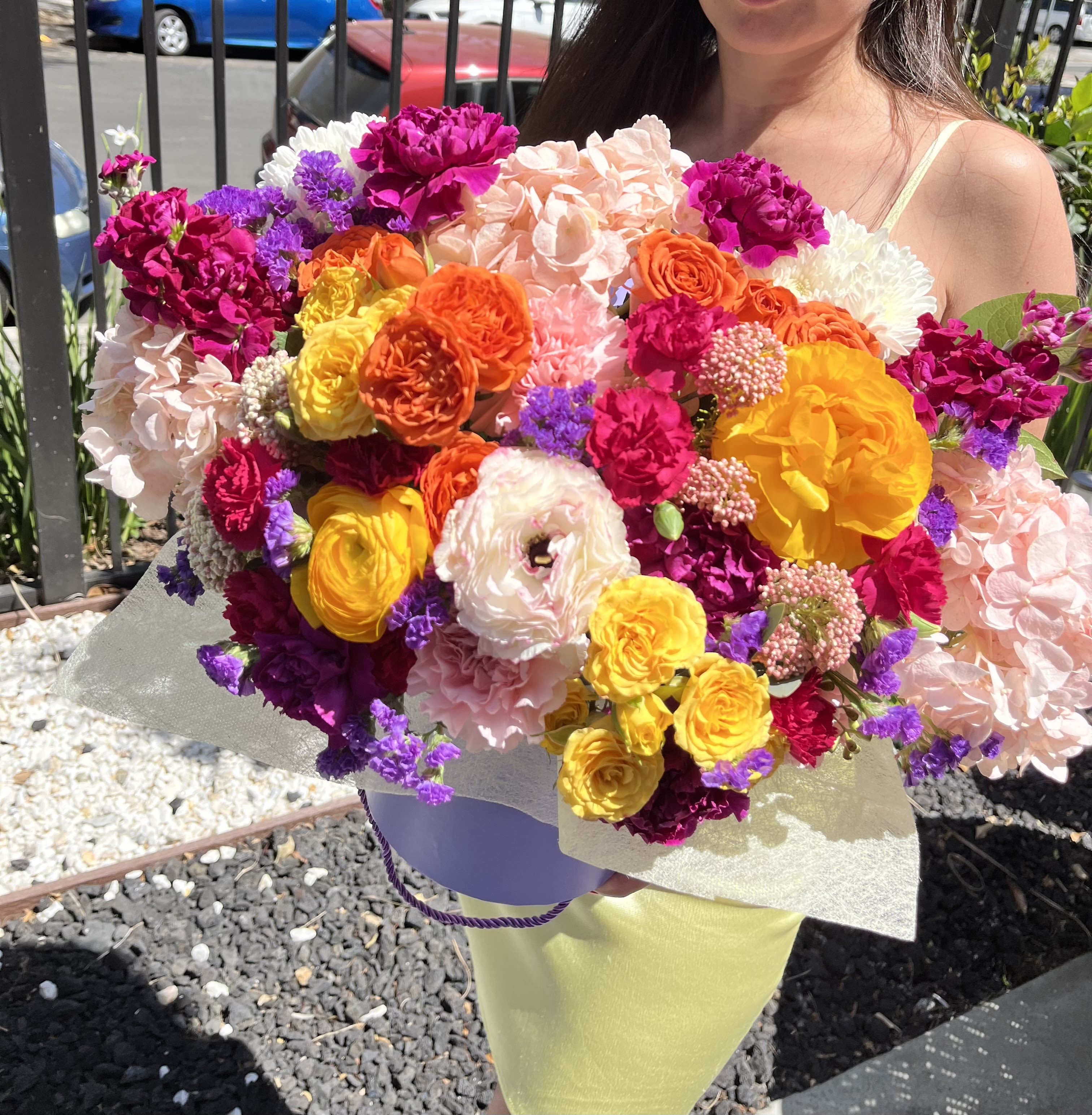 Electric Bloom - Bold, fearless, and full of life, Electric Bloom is a dazzling explosion of color designed to energize any space. This vibrant arrangement features fiery orange and golden yellow ranunculus, vivid magenta carnations, blush hydrangeas, hot pink roses, soft lisianthus, and pops of violet statice — all styled in a chic lavender hatbox.  Perfect for celebrations, grand gestures, or when you want your flowers to say “look at me.”  Style: Vibrant, modern, showstopping Fragrance: Bright, fresh, and floral
